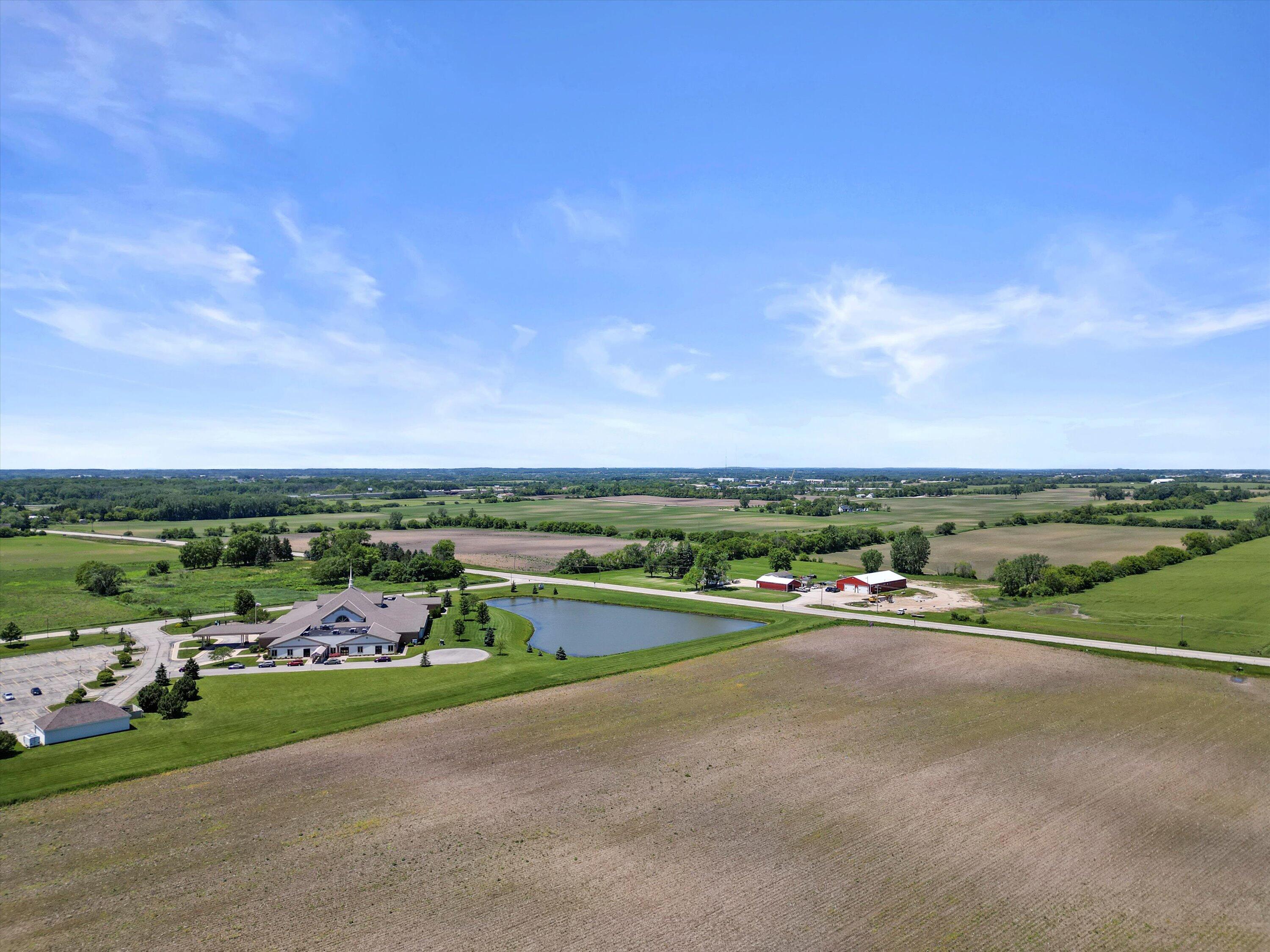 Aerial view of a large building and pond surrounded by farmland and open fields.