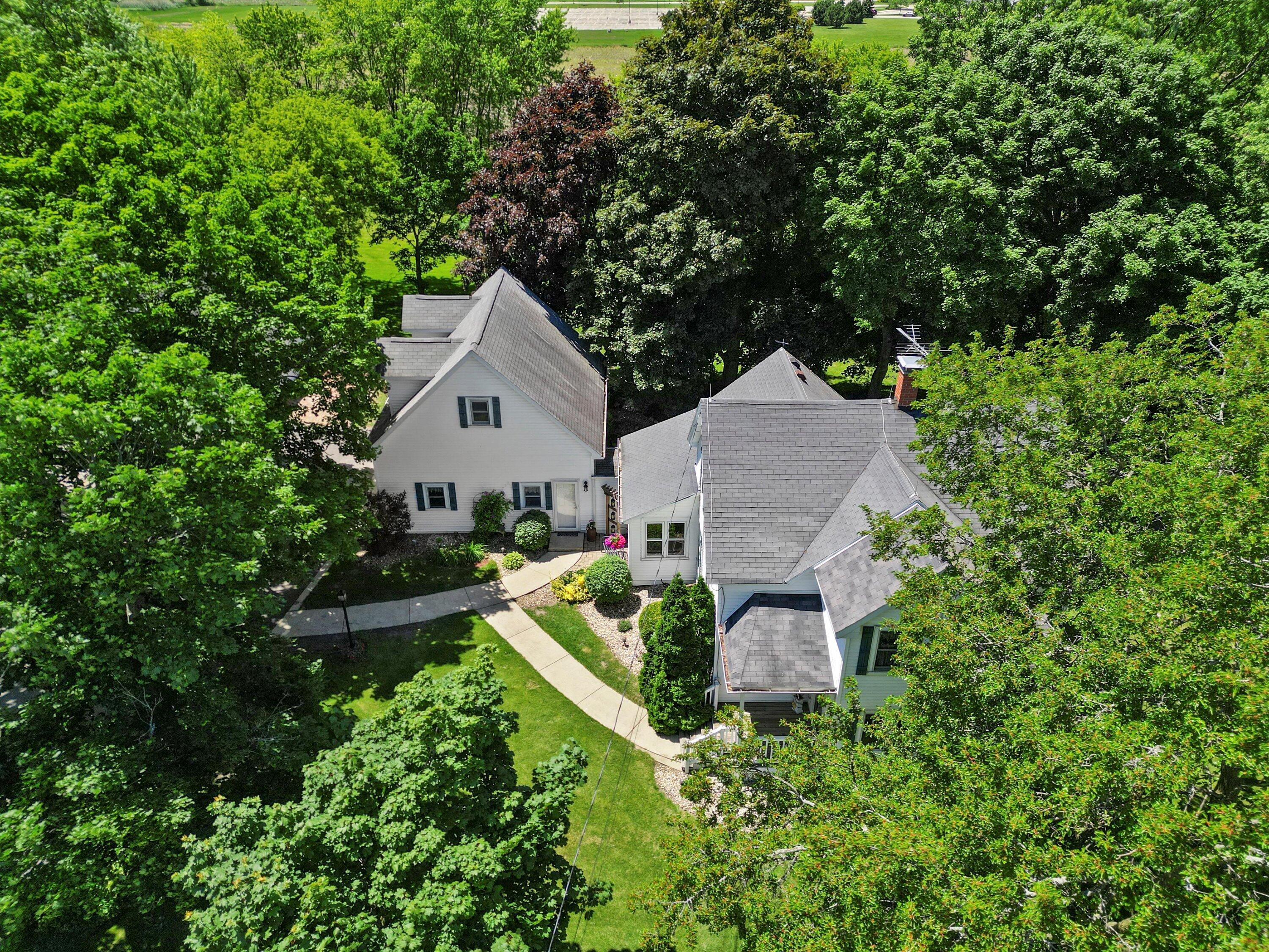 Aerial view of a white, multi-gabled house amid mature trees and landscaped grounds.