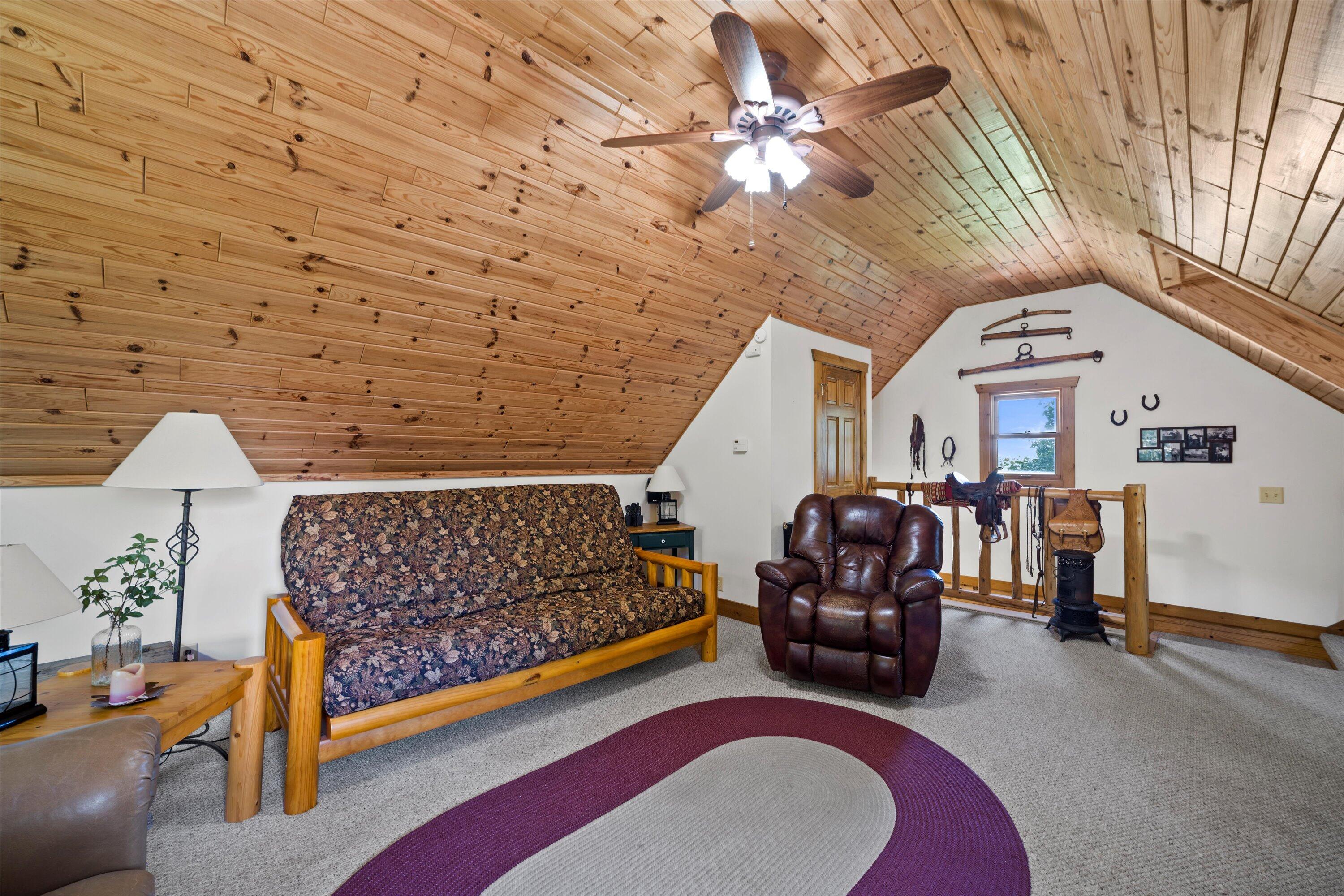 Attic sitting room with a sloped pine ceiling, patterned futon, and leather recliner.