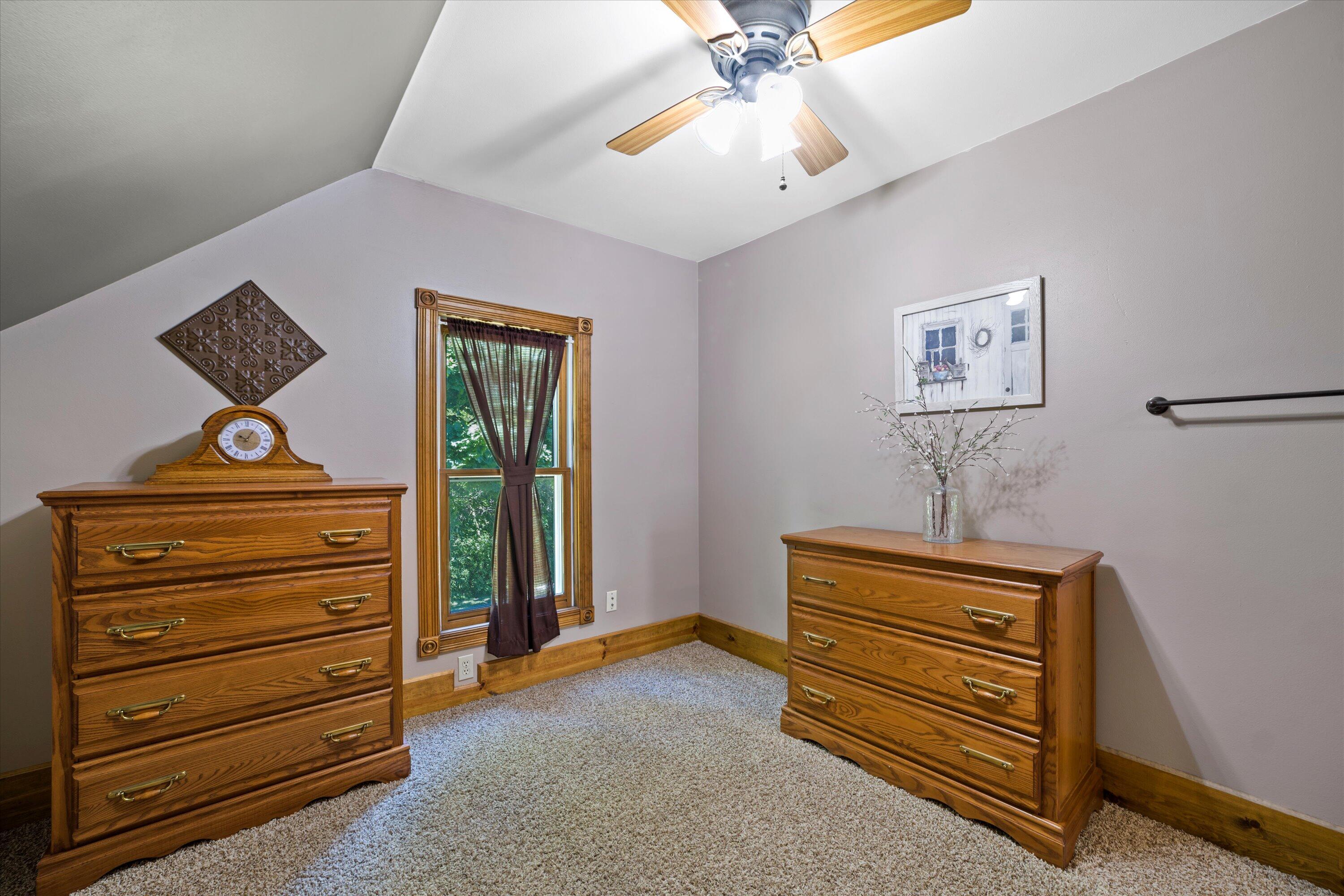 Furnished bedroom with a vaulted ceiling, wooden dressers, and a curtained window.