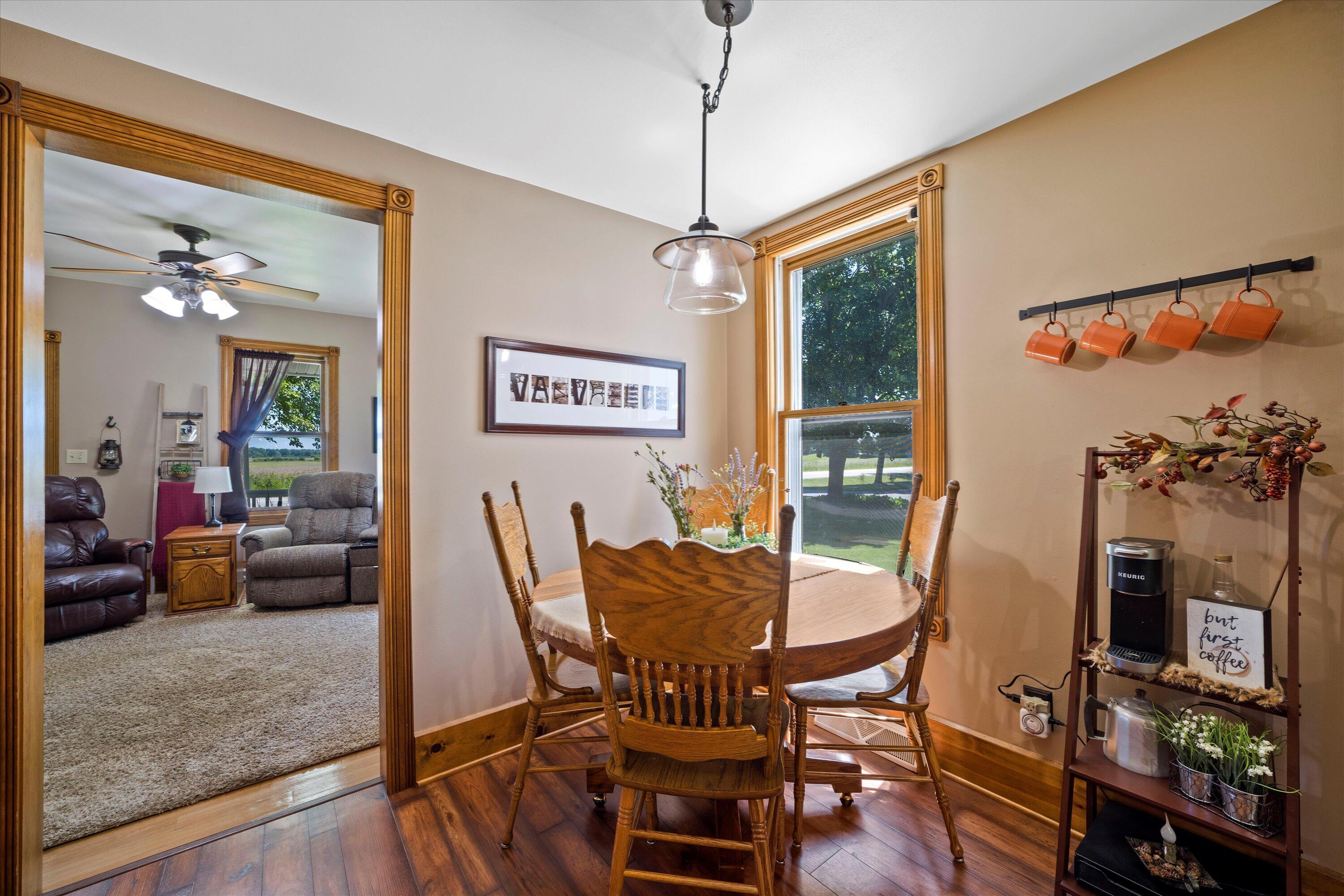 Dining area with a round wooden table beside a large window, opening to a carpeted living room.