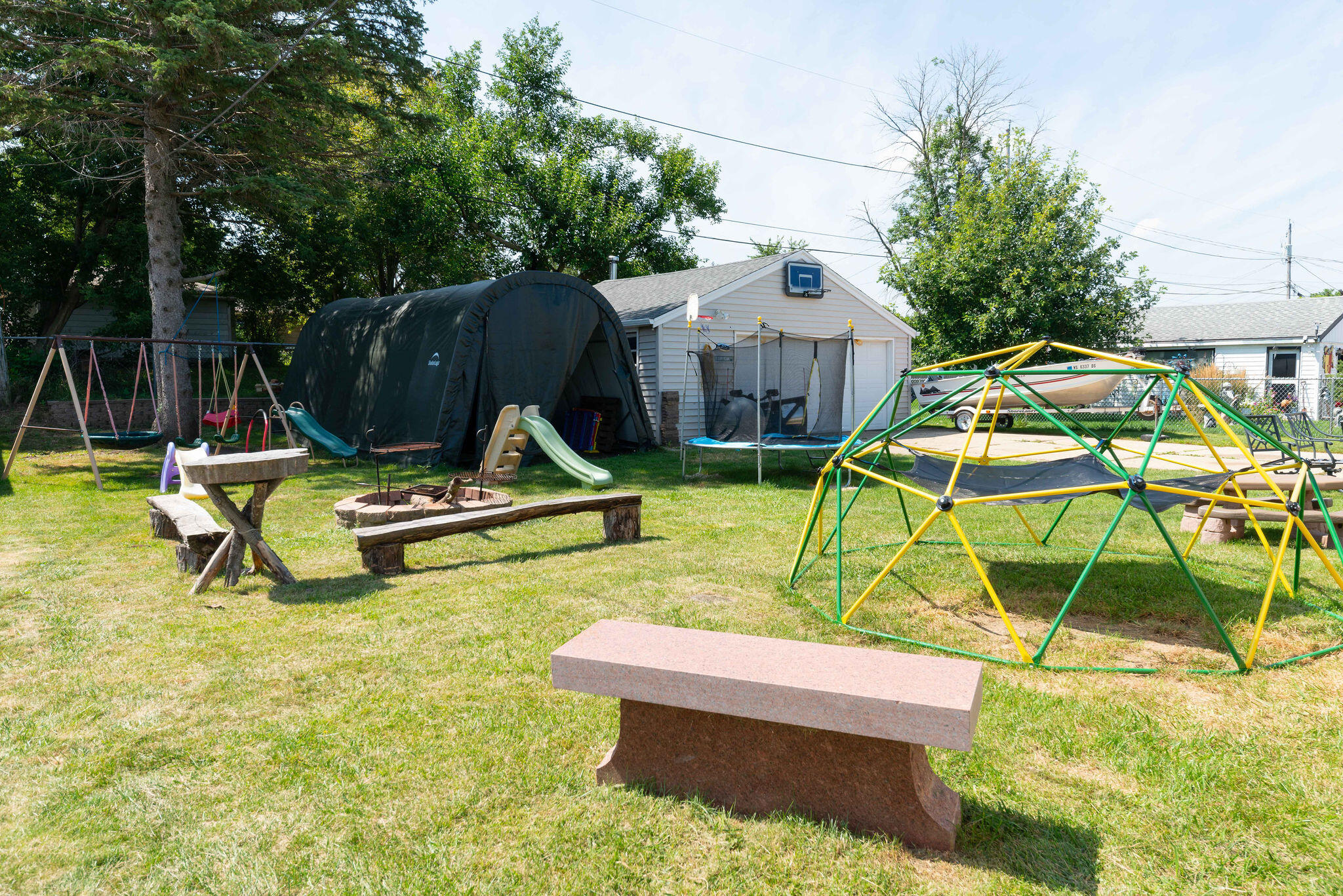 Backyard with a colorful climbing dome, swings, slides, and detached garage.