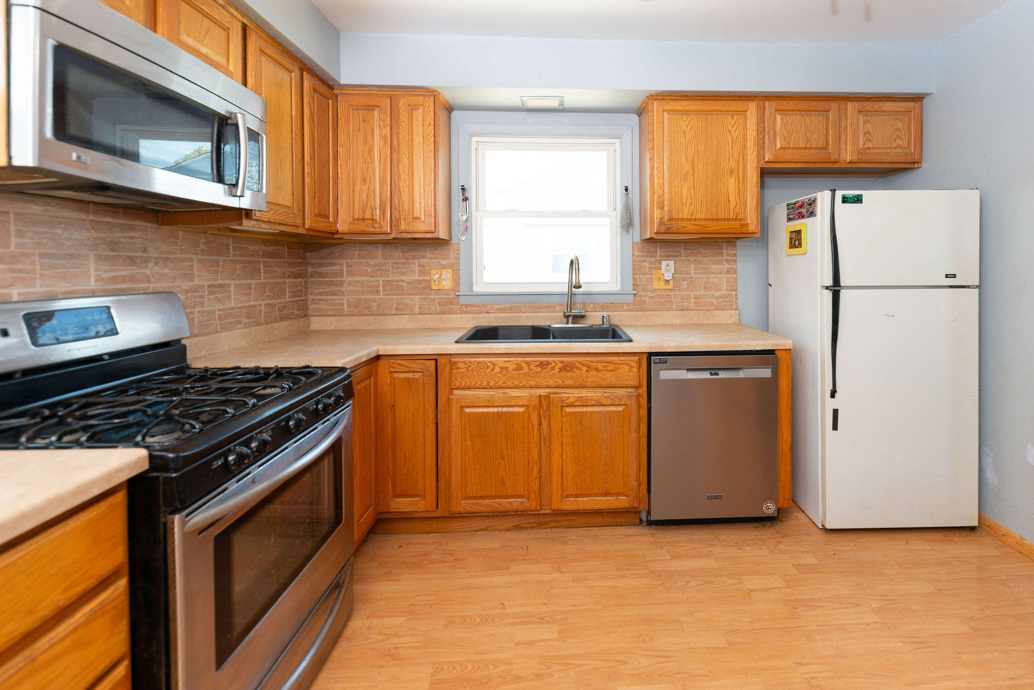 Kitchen with wood cabinets, brick backsplash, gas range, and sink beneath a window.