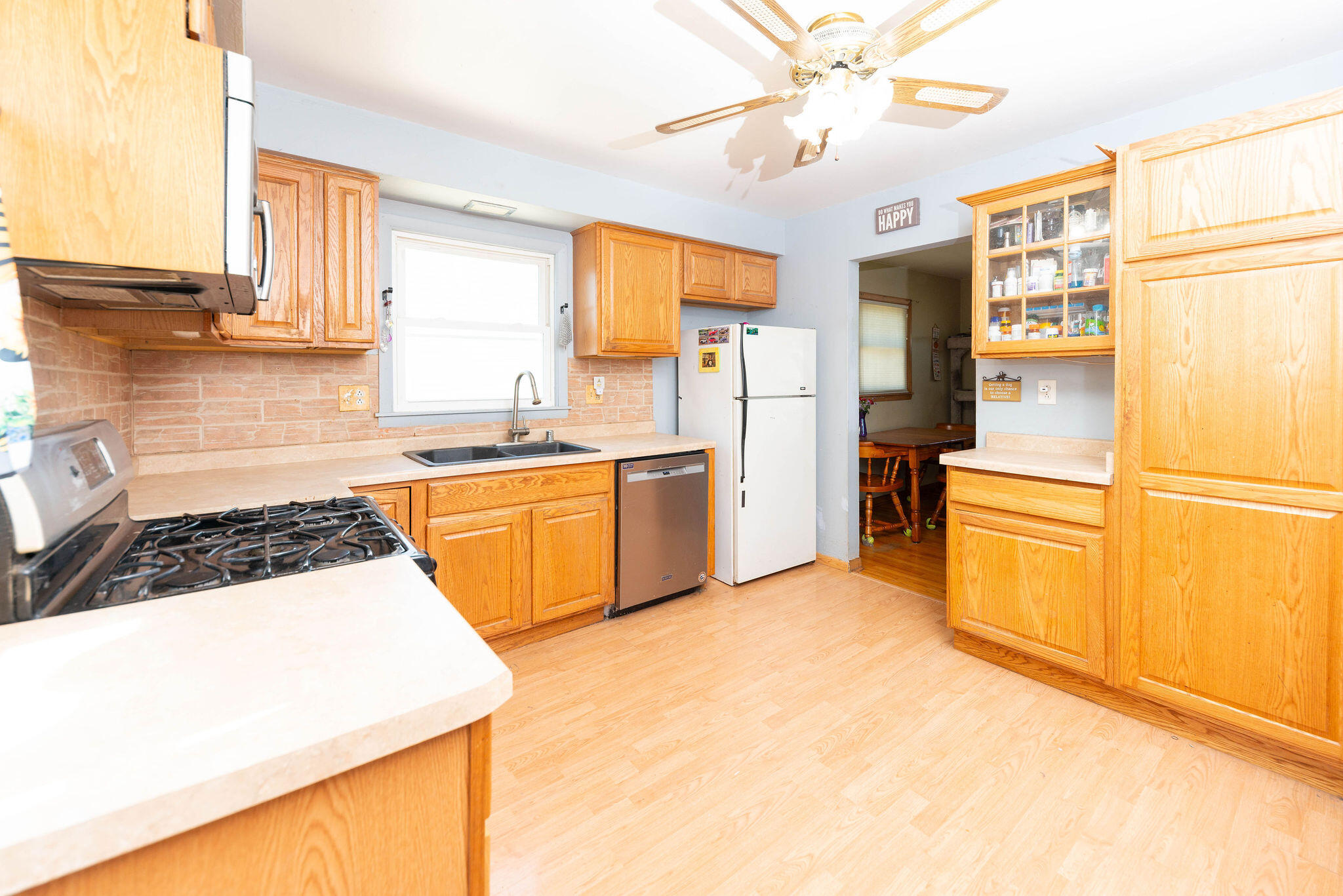 Kitchen with honey-colored cabinets, gas range, and sink beneath a window; doorway opens to a dining area.