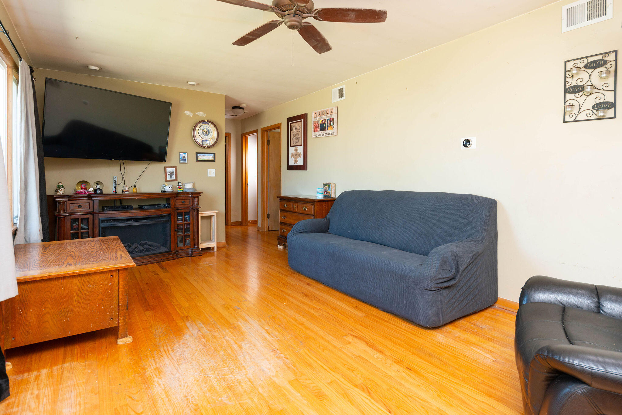 Living room with hardwood floors, a blue sofa, and a large television above a wood fireplace console.