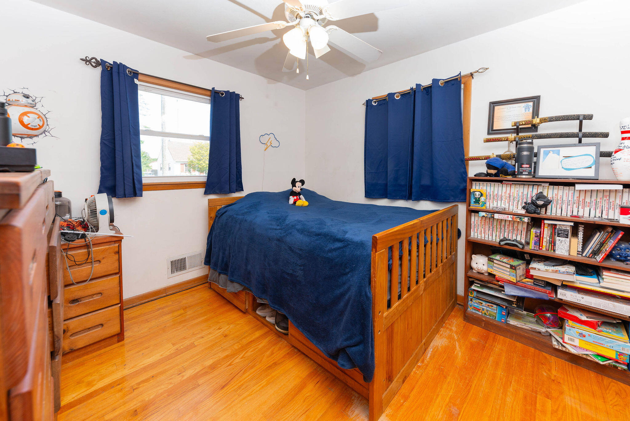 Bedroom with a wooden bed, navy curtains, hardwood floors, and a full bookshelf.