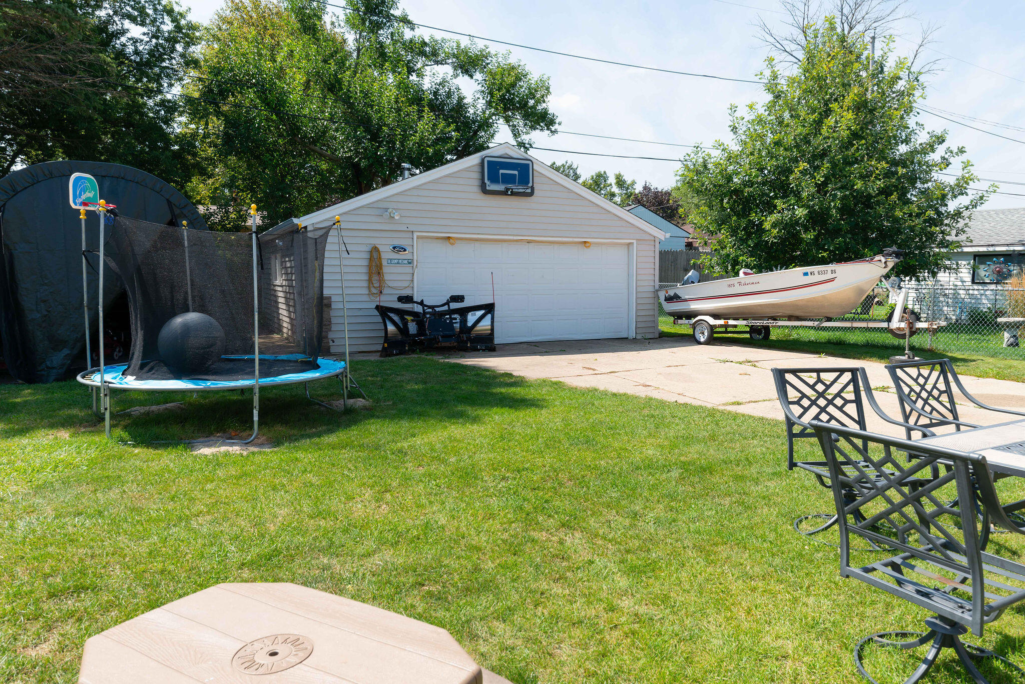 Backyard with a detached two-car garage, boat on a trailer, trampoline, and lawn seating.