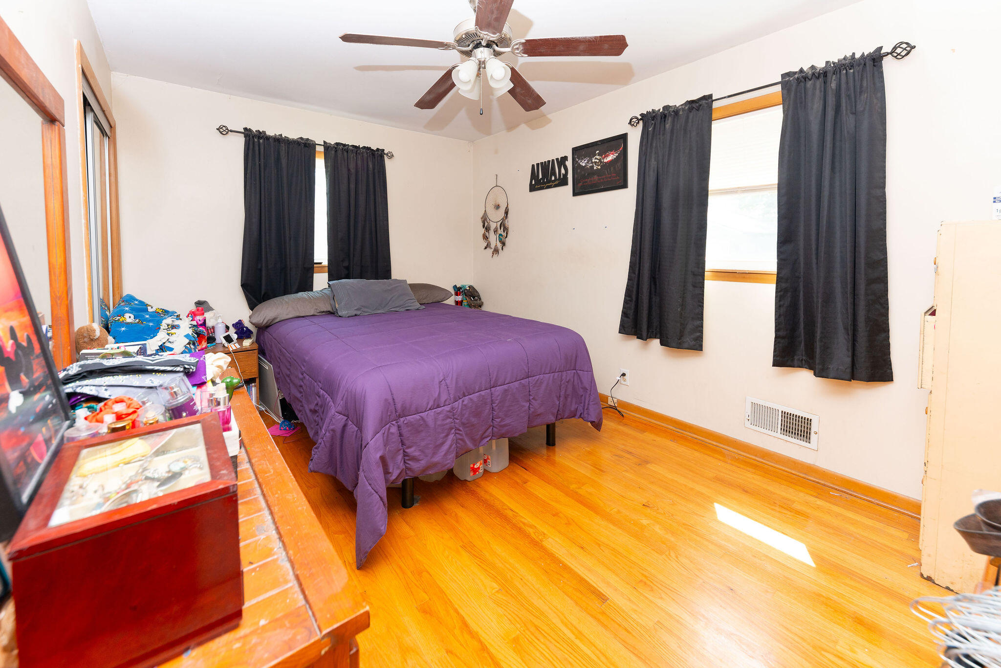Bedroom with a purple bedspread, dark curtains, and hardwood floors.