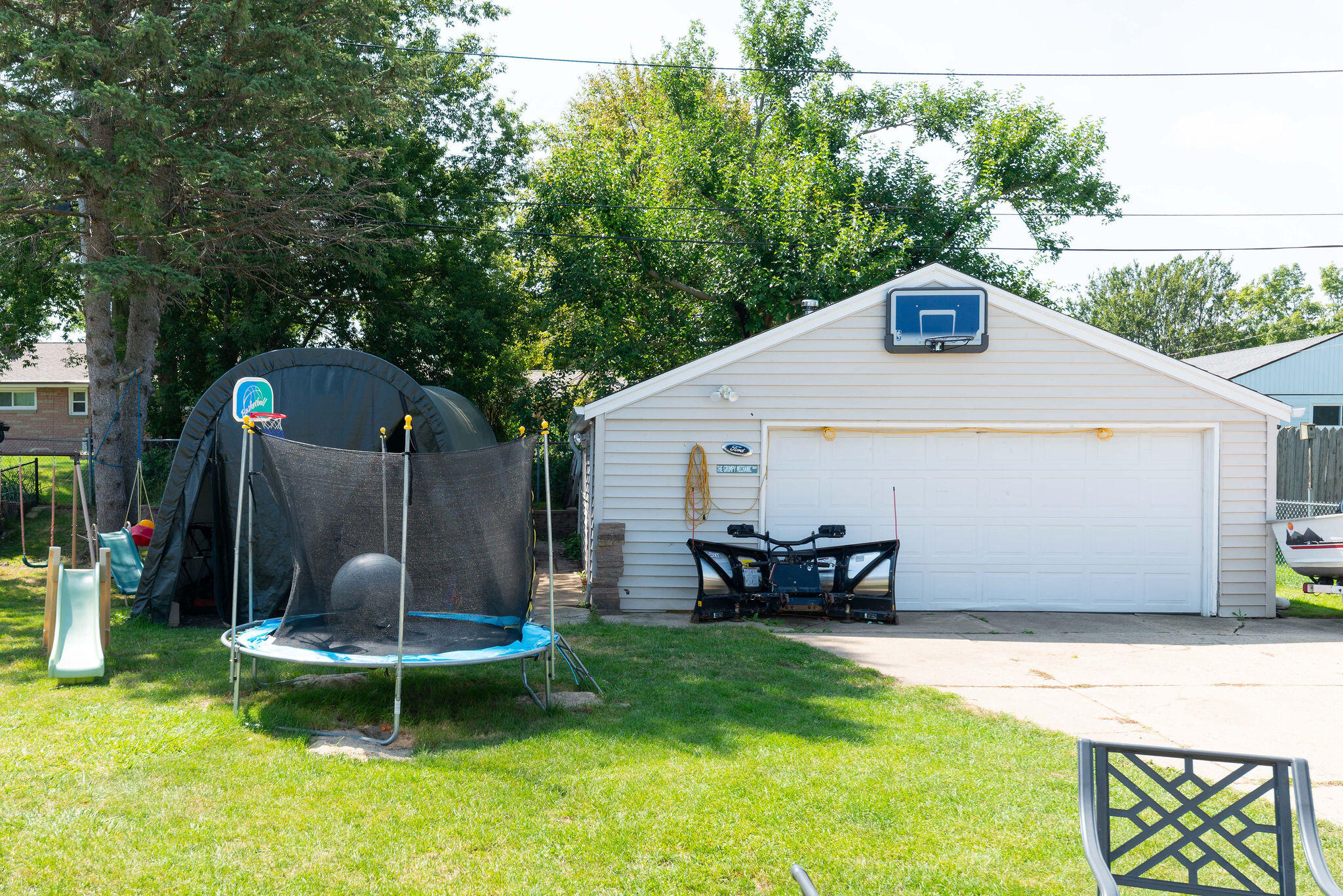 Backyard with a white garage, basketball hoop, trampoline, and children’s play slide.