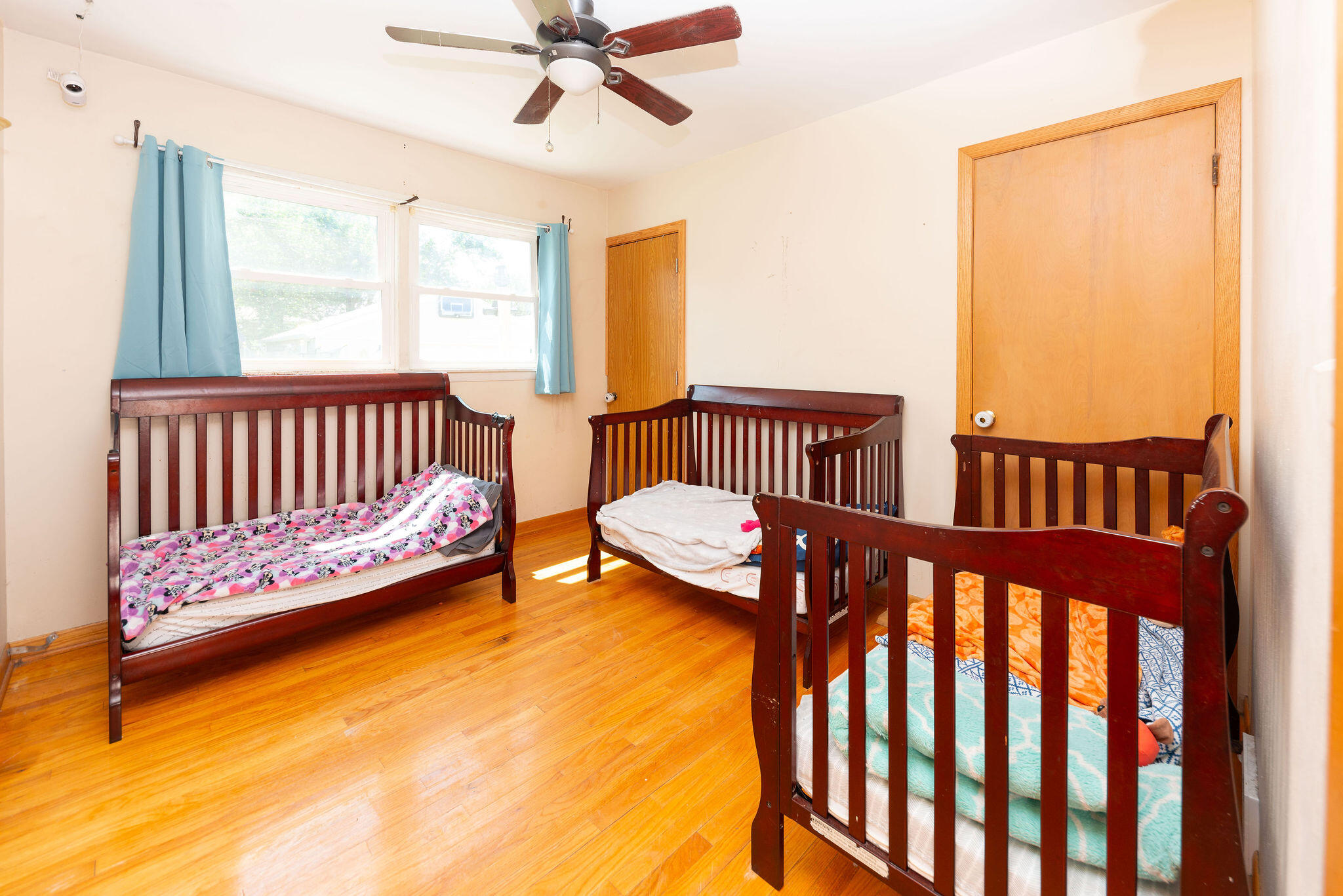 Bedroom with three dark wood cribs, colorful bedding, and hardwood floors.