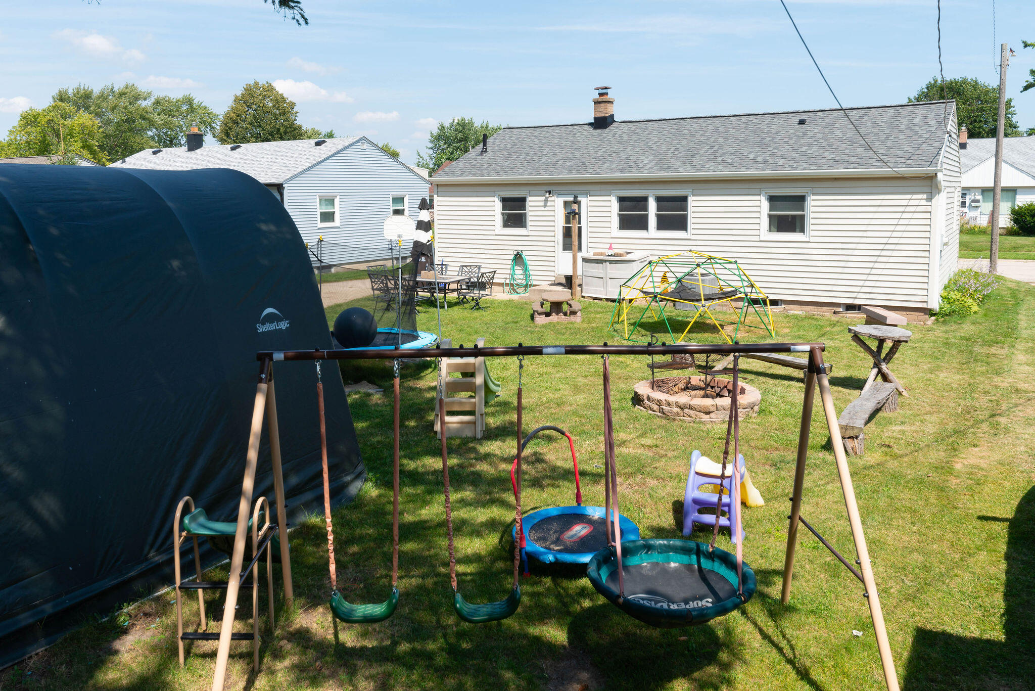 Rear of the house with a grassy yard, playset, swings, trampoline, and stone fire pit.