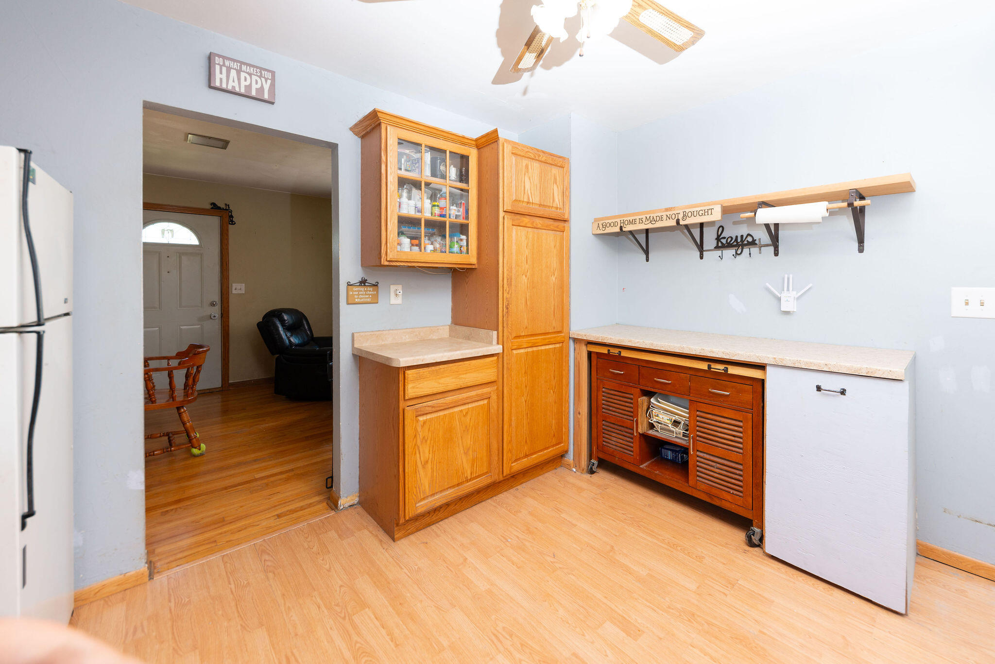 Kitchen with honey-colored cabinets and a long countertop beside an open doorway to the entry.
