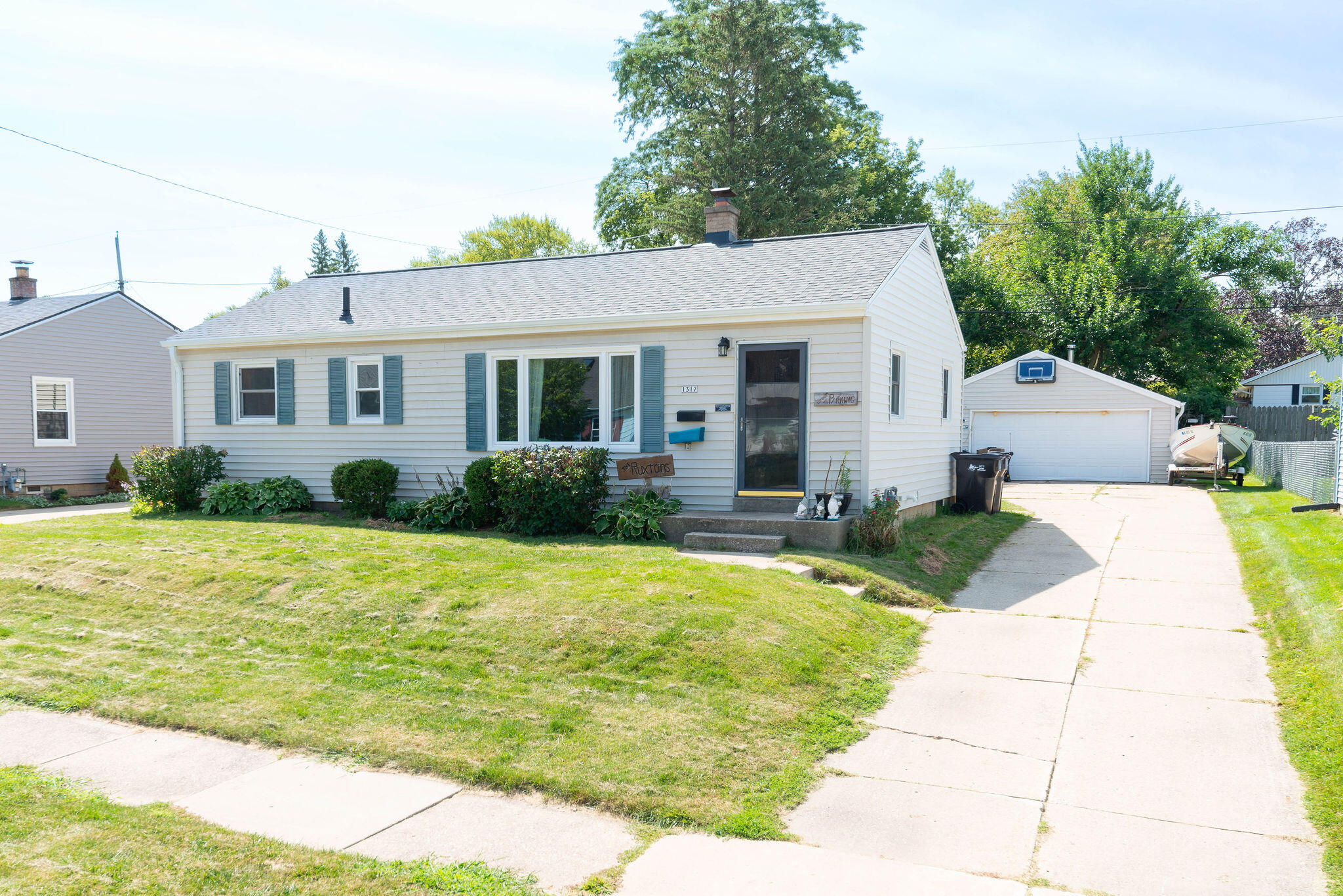 White single-story home with blue shutters, front garden, driveway, and detached garage.