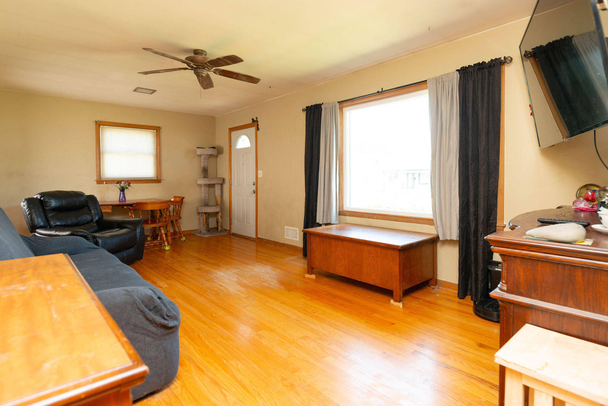 Living room with hardwood floors, leather seating, and a large window with dark and light curtains.