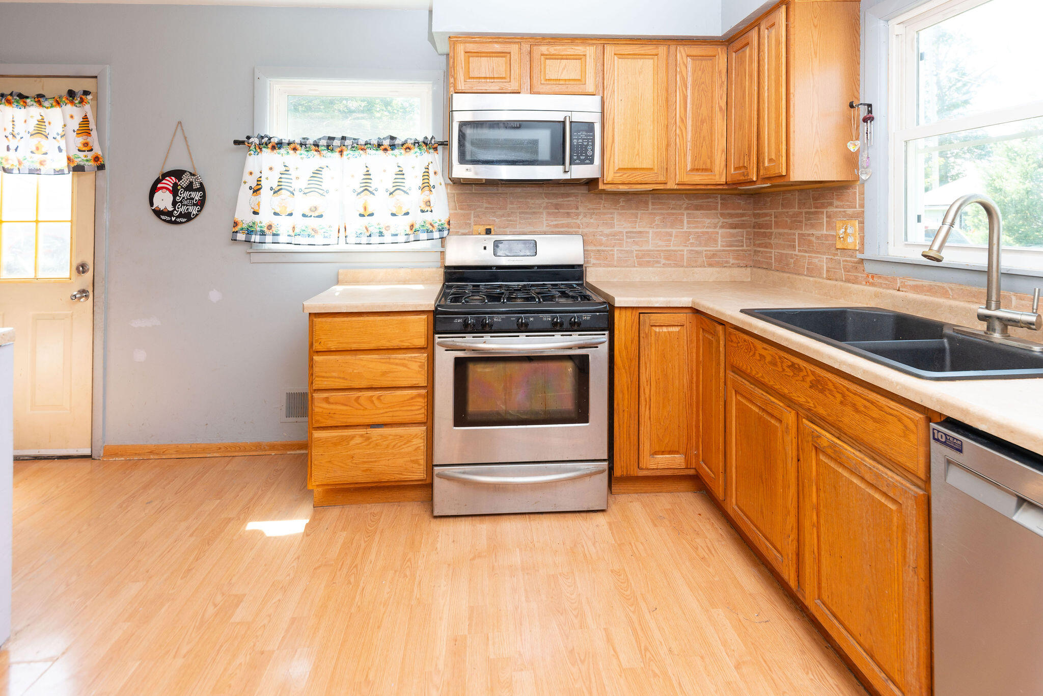 Kitchen with honey-colored cabinets, stainless steel range, brick backsplash, and black double sink beneath a window.