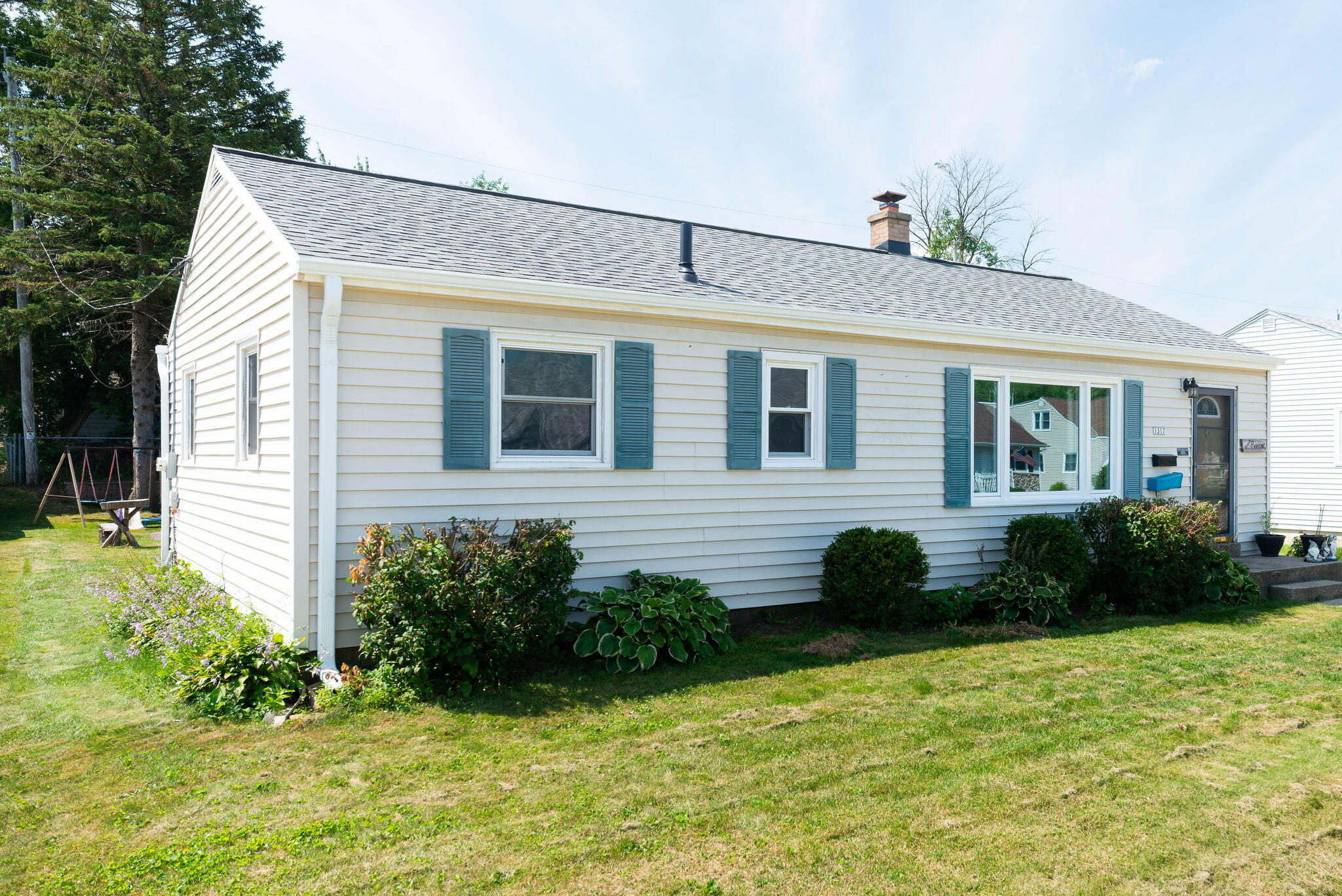 White single-story home with blue shutters, a front lawn, and landscaped shrubs.