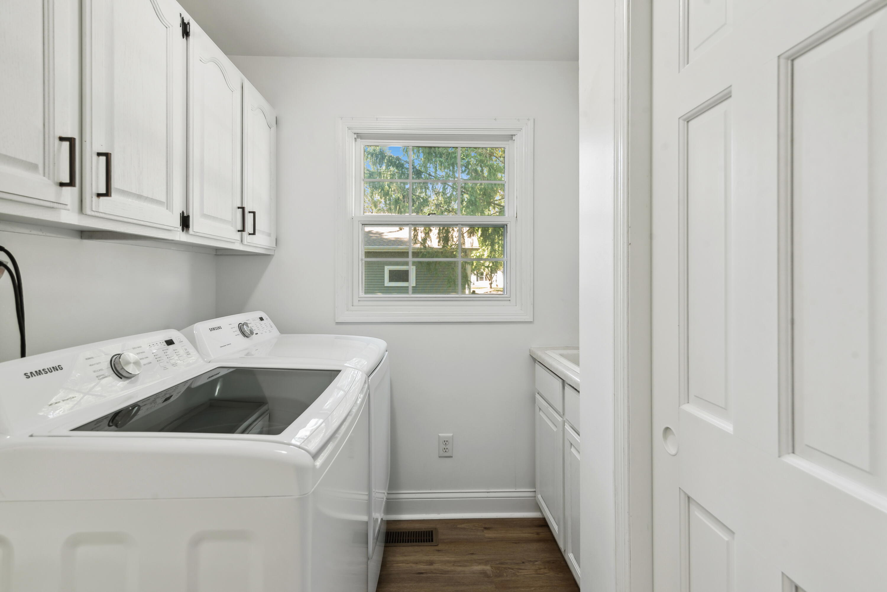 Laundry room with white washer and dryer beneath cabinets and a window.