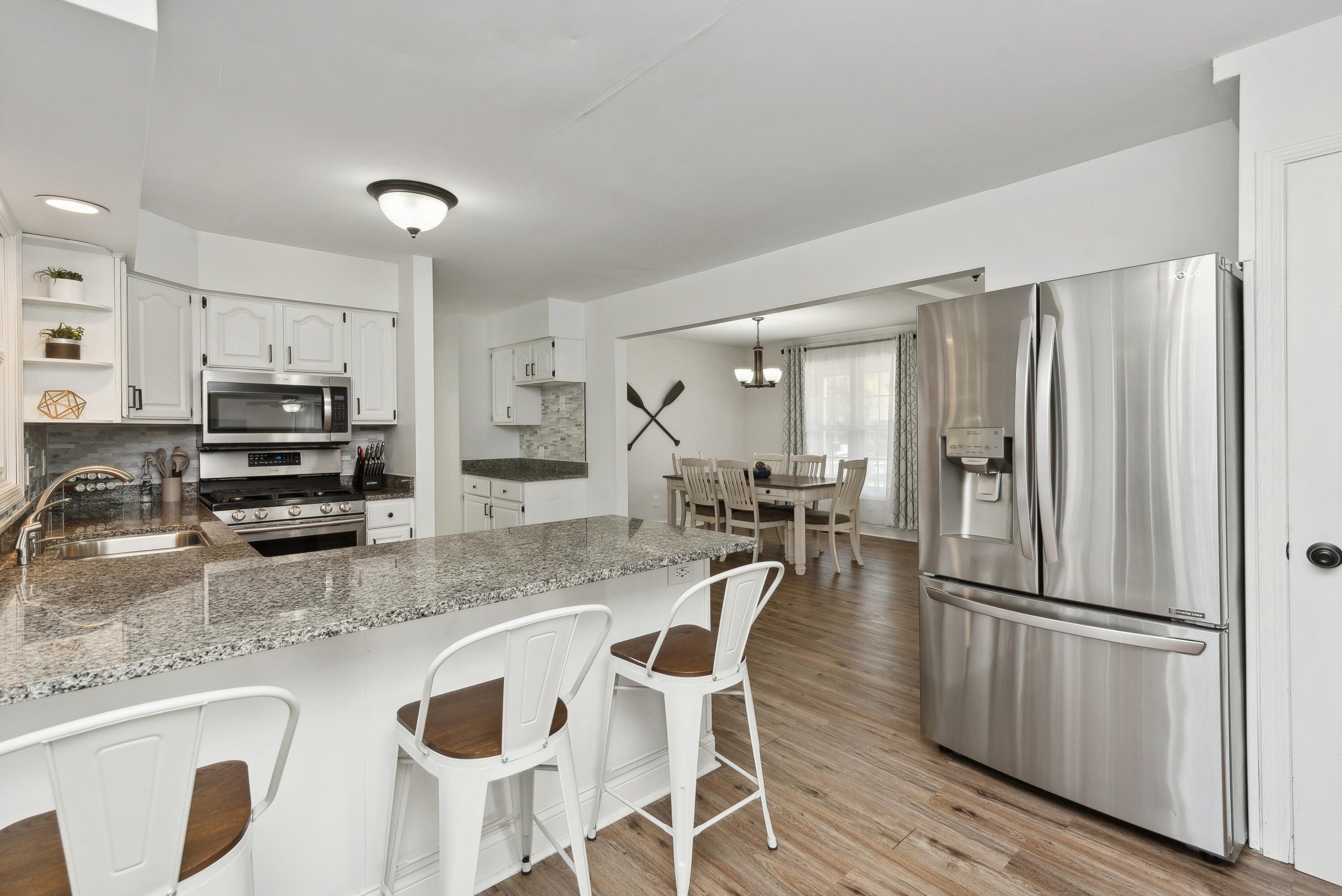 Kitchen with a granite island, stainless steel appliances, white cabinetry, and an adjoining dining area.