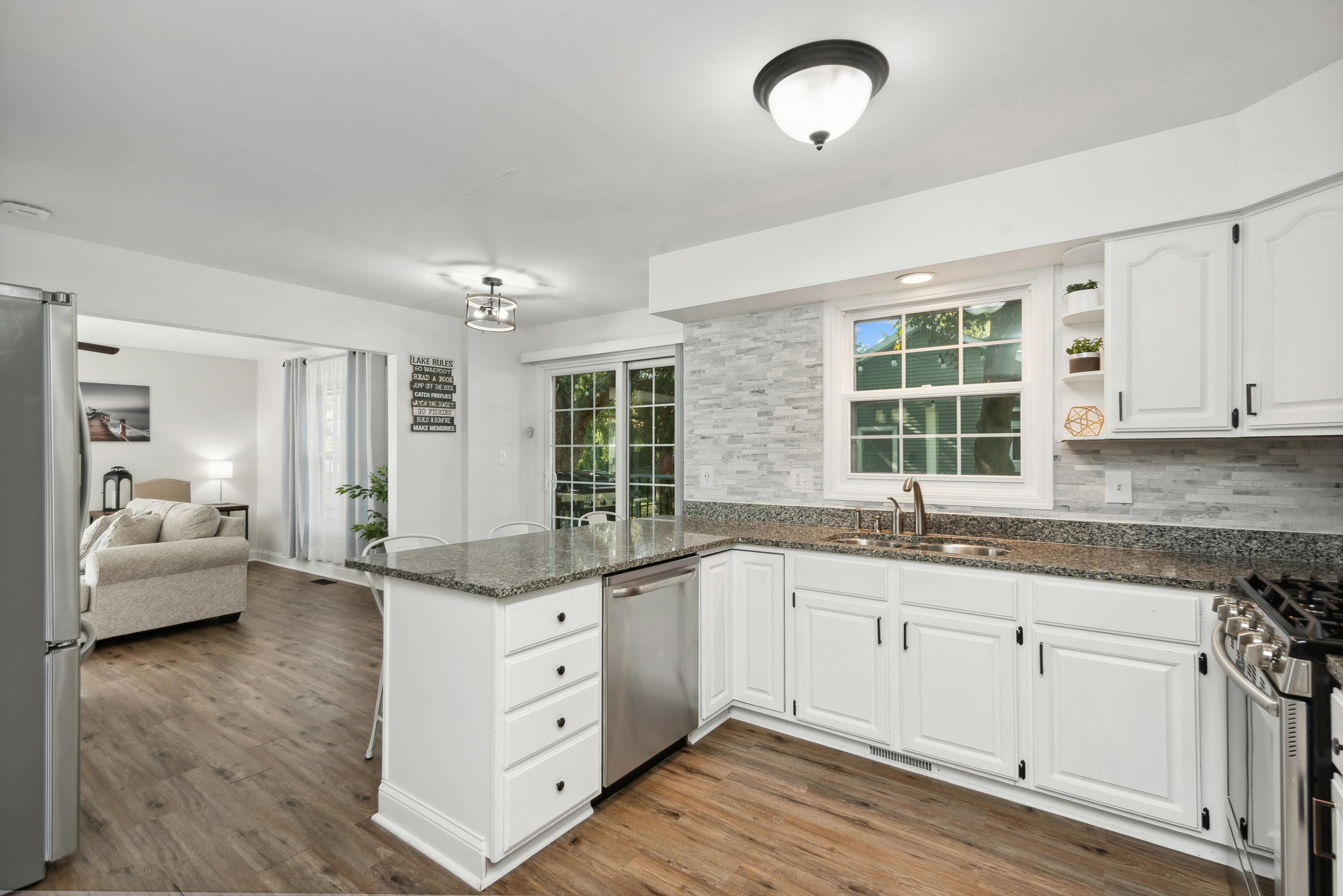 Bright white kitchen with granite island, stainless steel appliances, and an open connection to the living room.