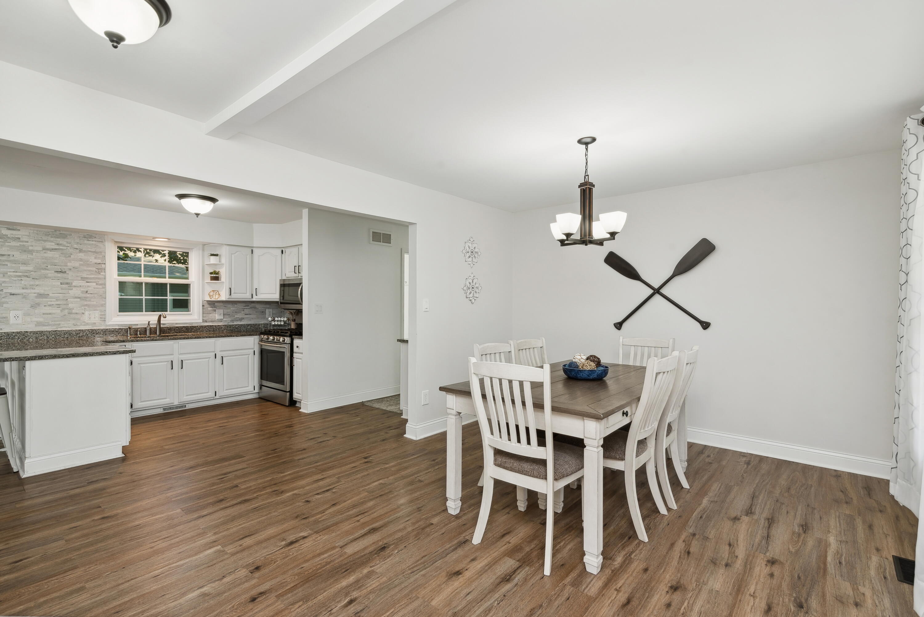 Dining area with a dark wood table and white chairs beside a bright kitchen.