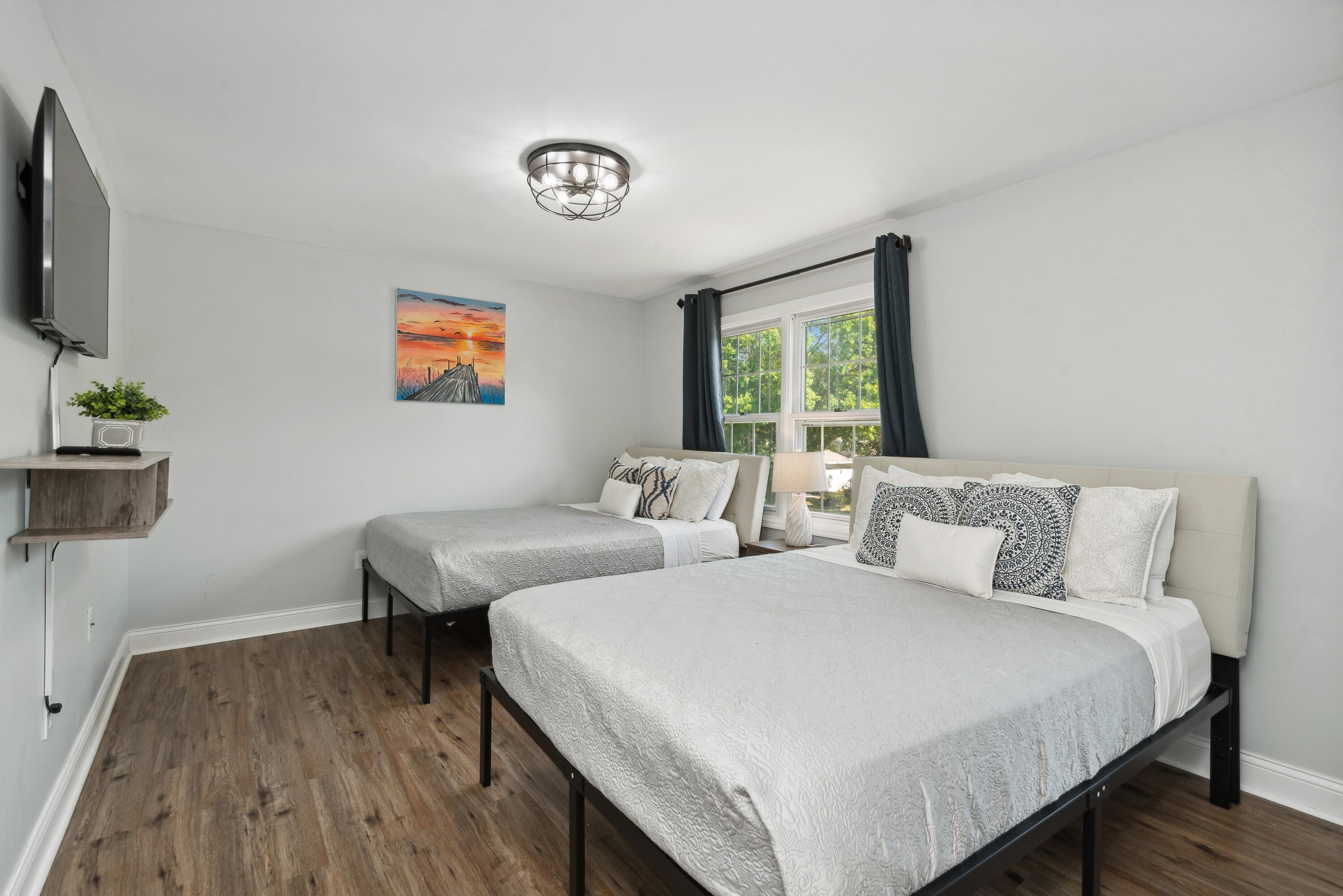 Bedroom with two beds, dark curtains, and a window overlooking green trees.