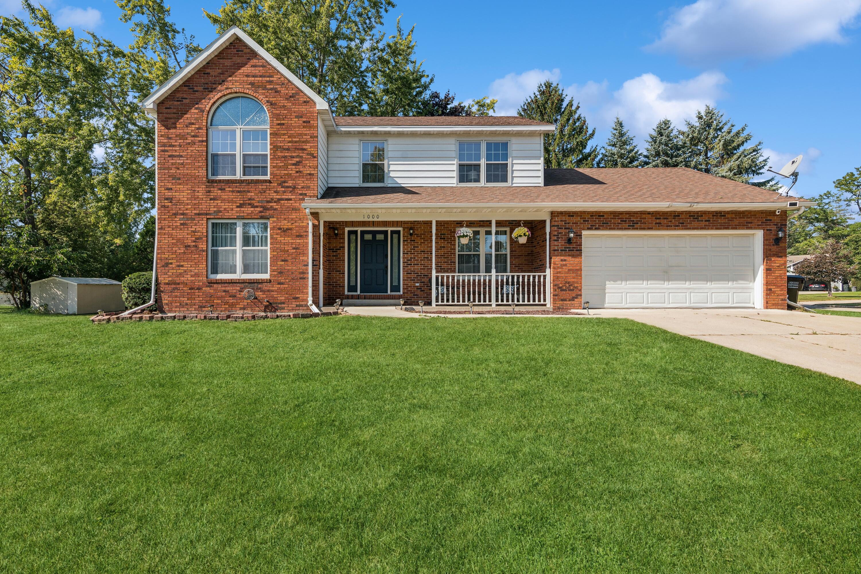 Two-story brick-and-siding home with a covered porch, attached garage, and broad lawn.