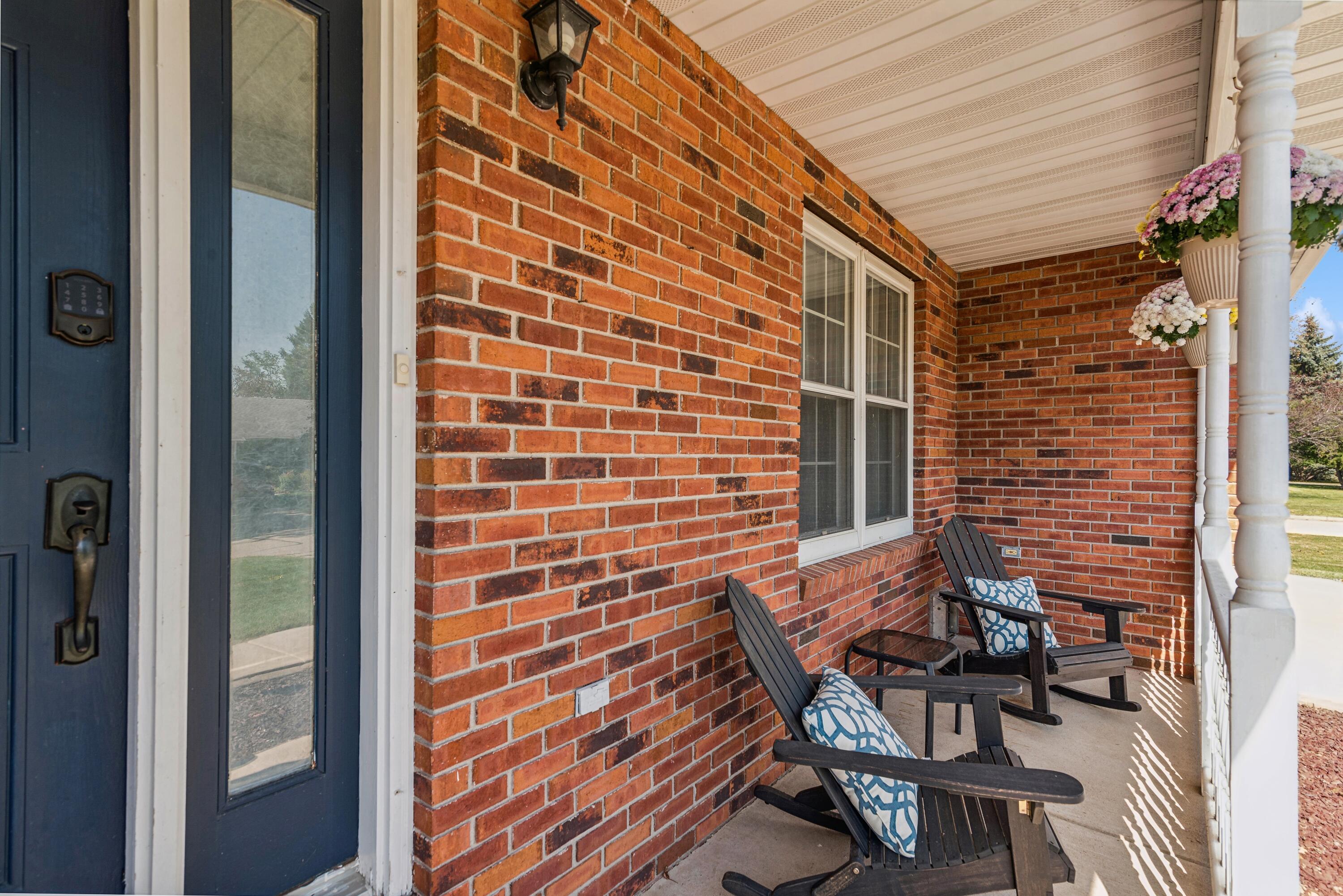 Covered brick front porch with a blue door, rocking chairs, and hanging flower planters.