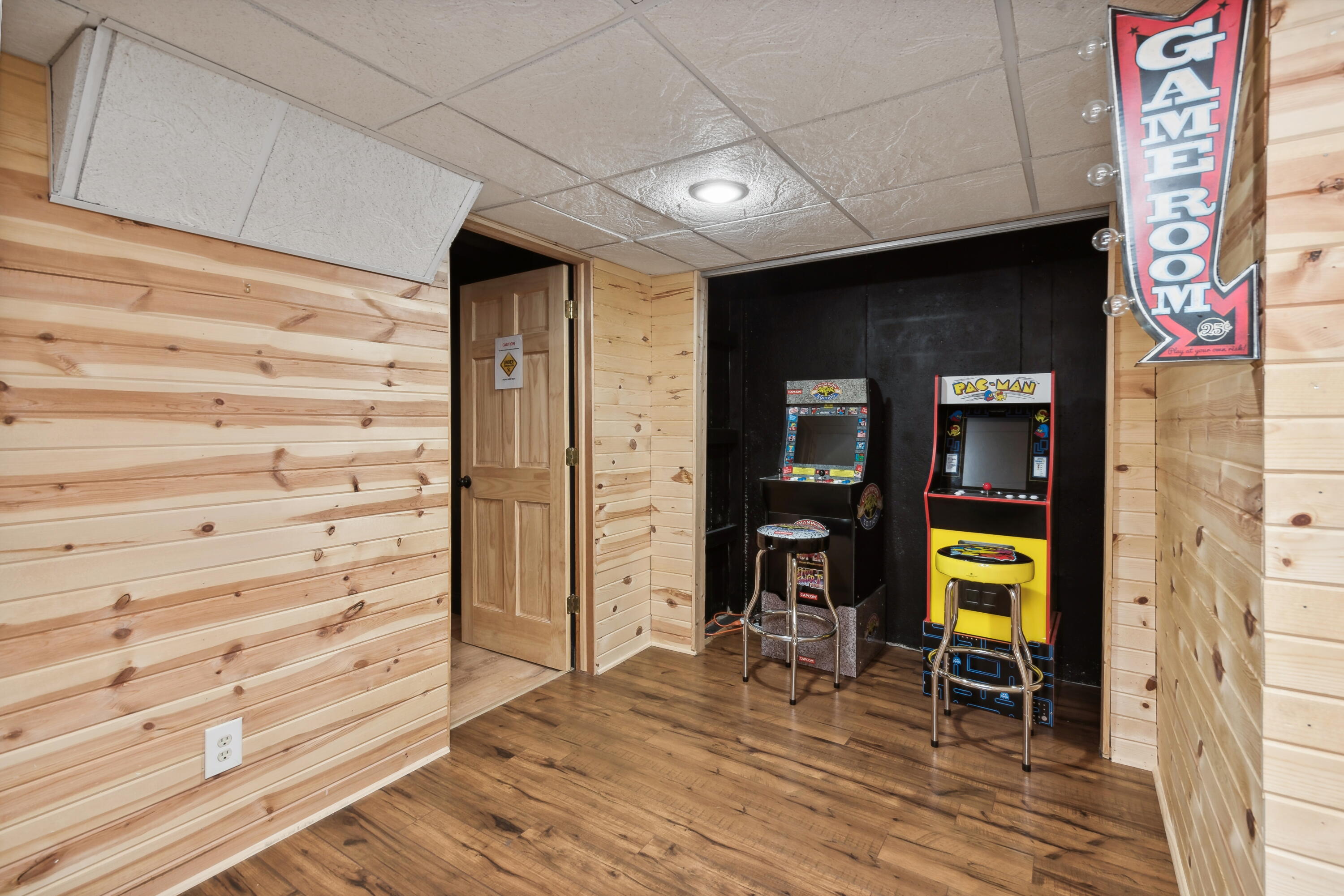 Game room with two arcade cabinets, wood-plank walls, and a GAME ROOM sign.