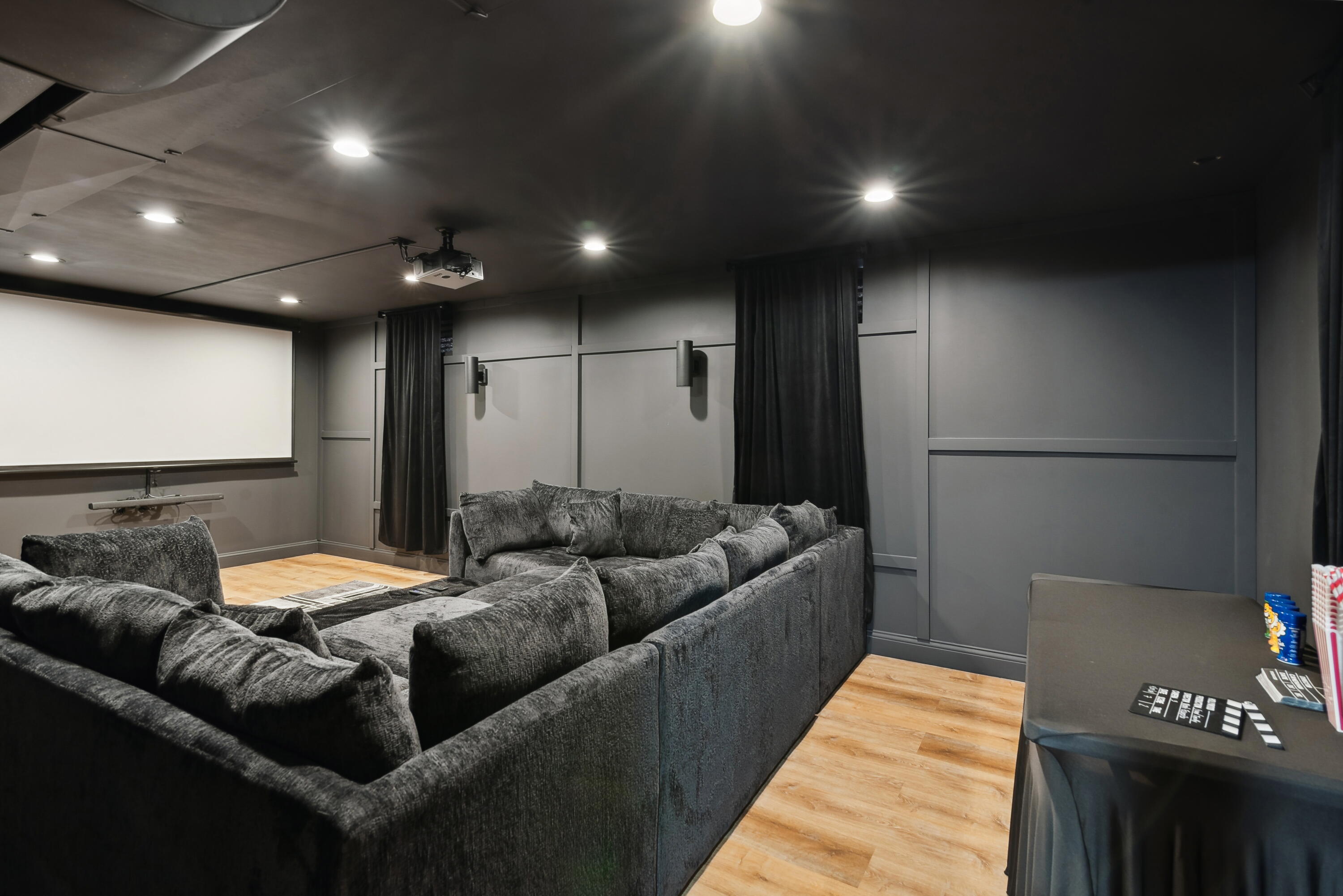 Home theater with a large projection screen, ceiling projector, and charcoal sectional sofa.