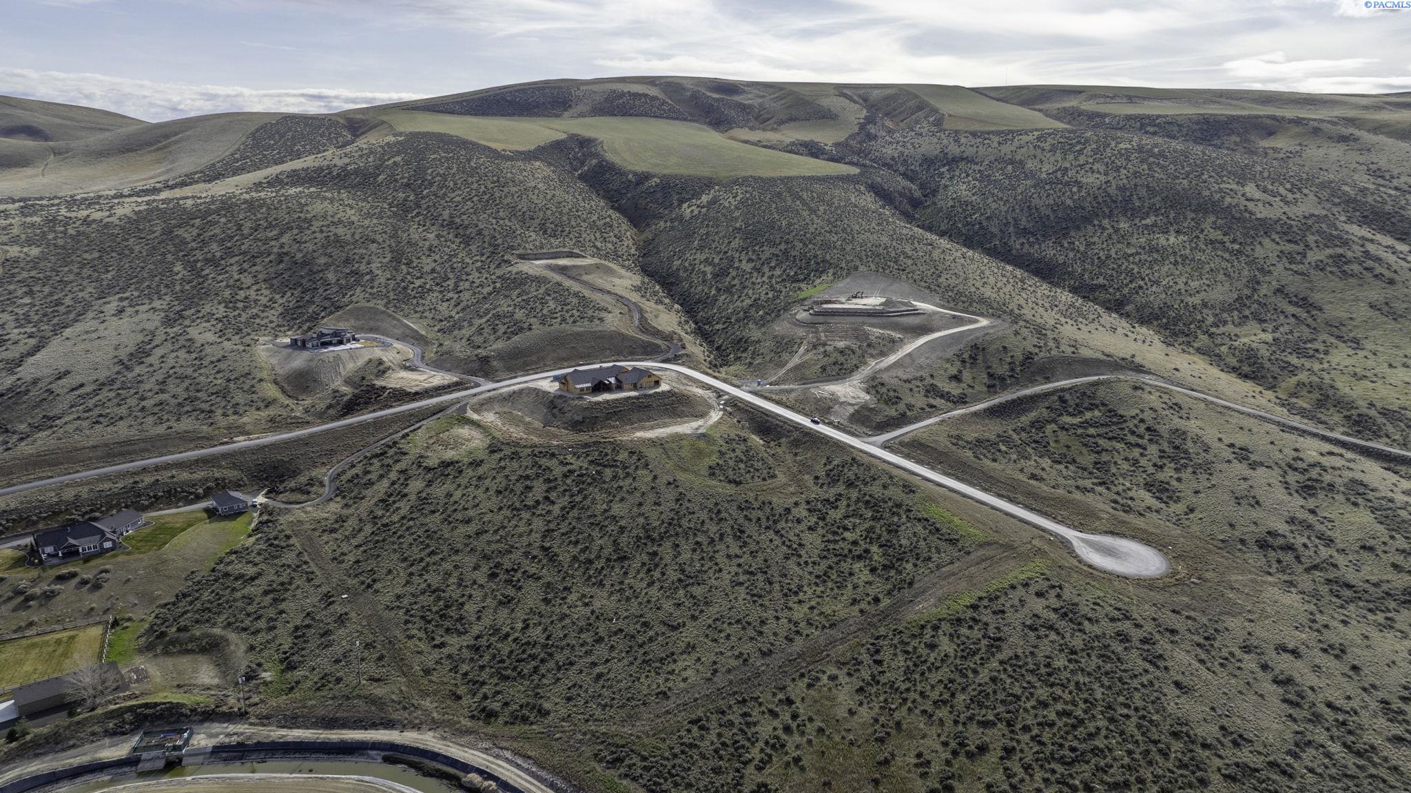 Aerial view of homes and winding roads among rolling, shrub-covered hills.