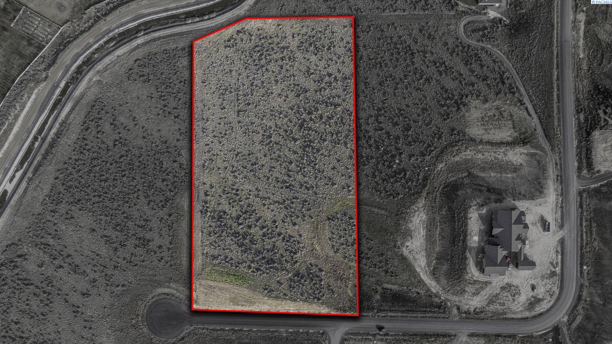 Aerial view of scrub-covered vacant land outlined in red beside a road and neighboring house.