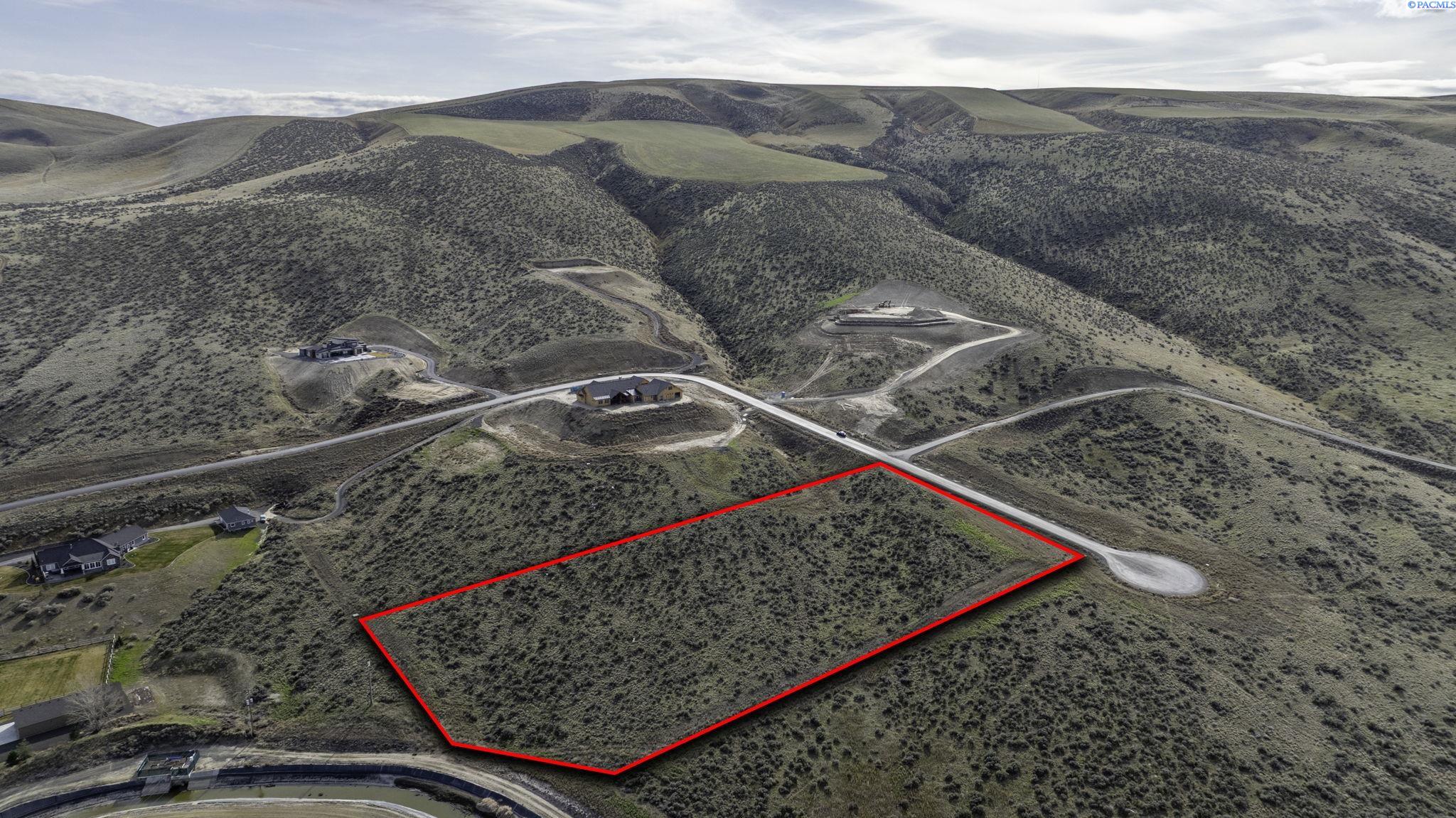 Aerial view of a vacant, scrub-covered parcel outlined in red among rolling hills and nearby homes.