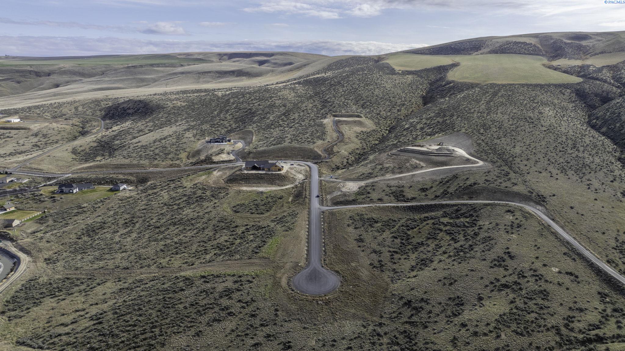 Aerial view of rolling hills, winding roads, scattered homes, and graded building sites.