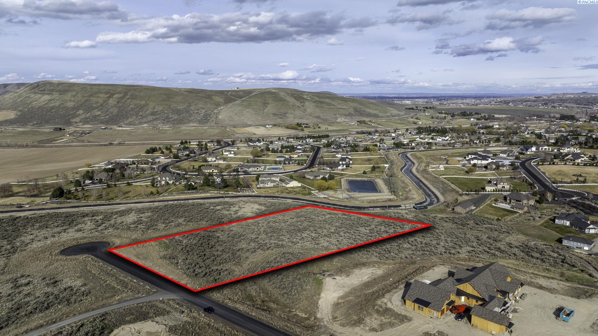 Aerial view of a vacant hillside lot outlined in red beside a residential development.
