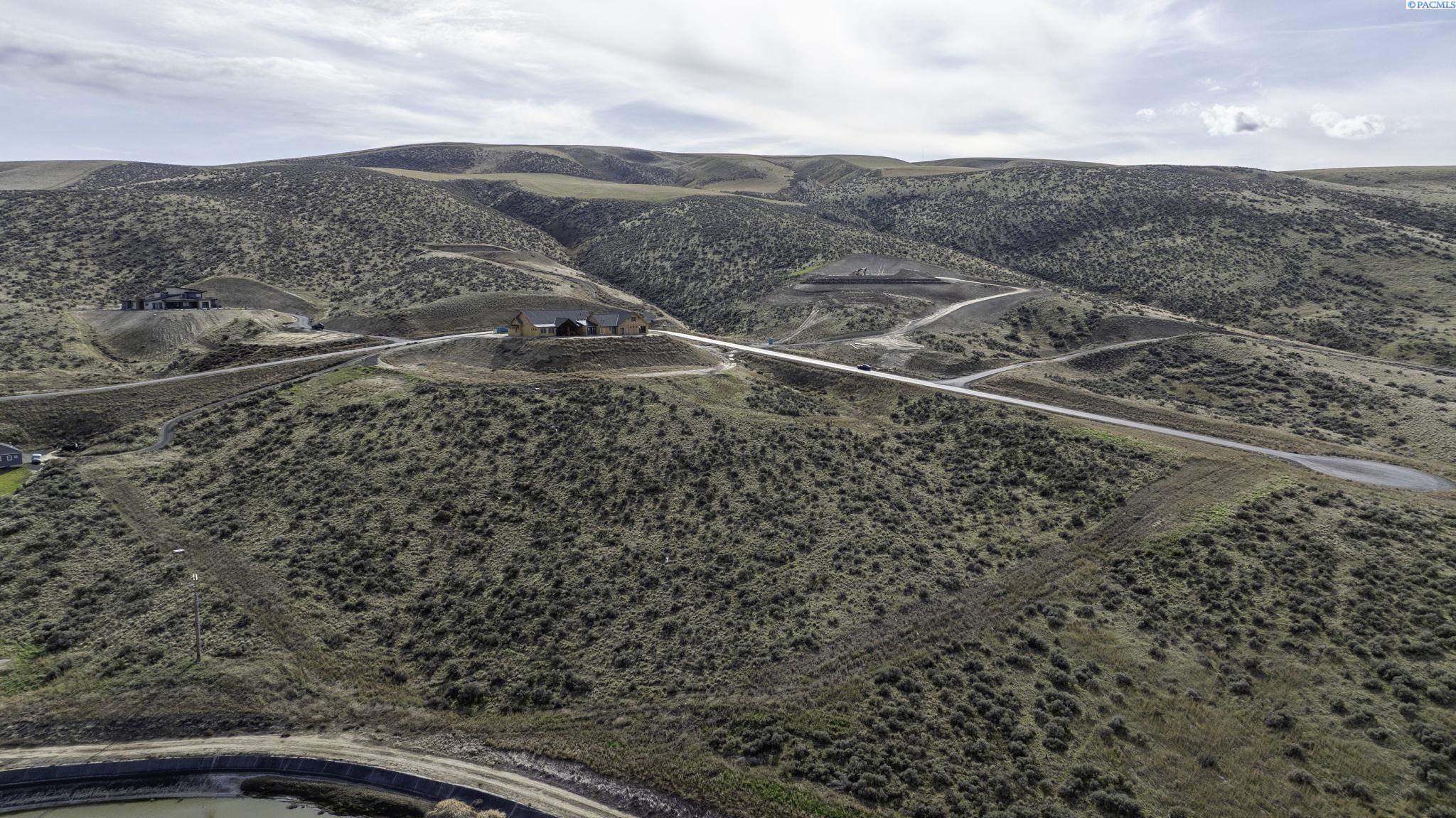Aerial view of homes amid rolling scrubland, with winding roads and a narrow waterway in the foreground.