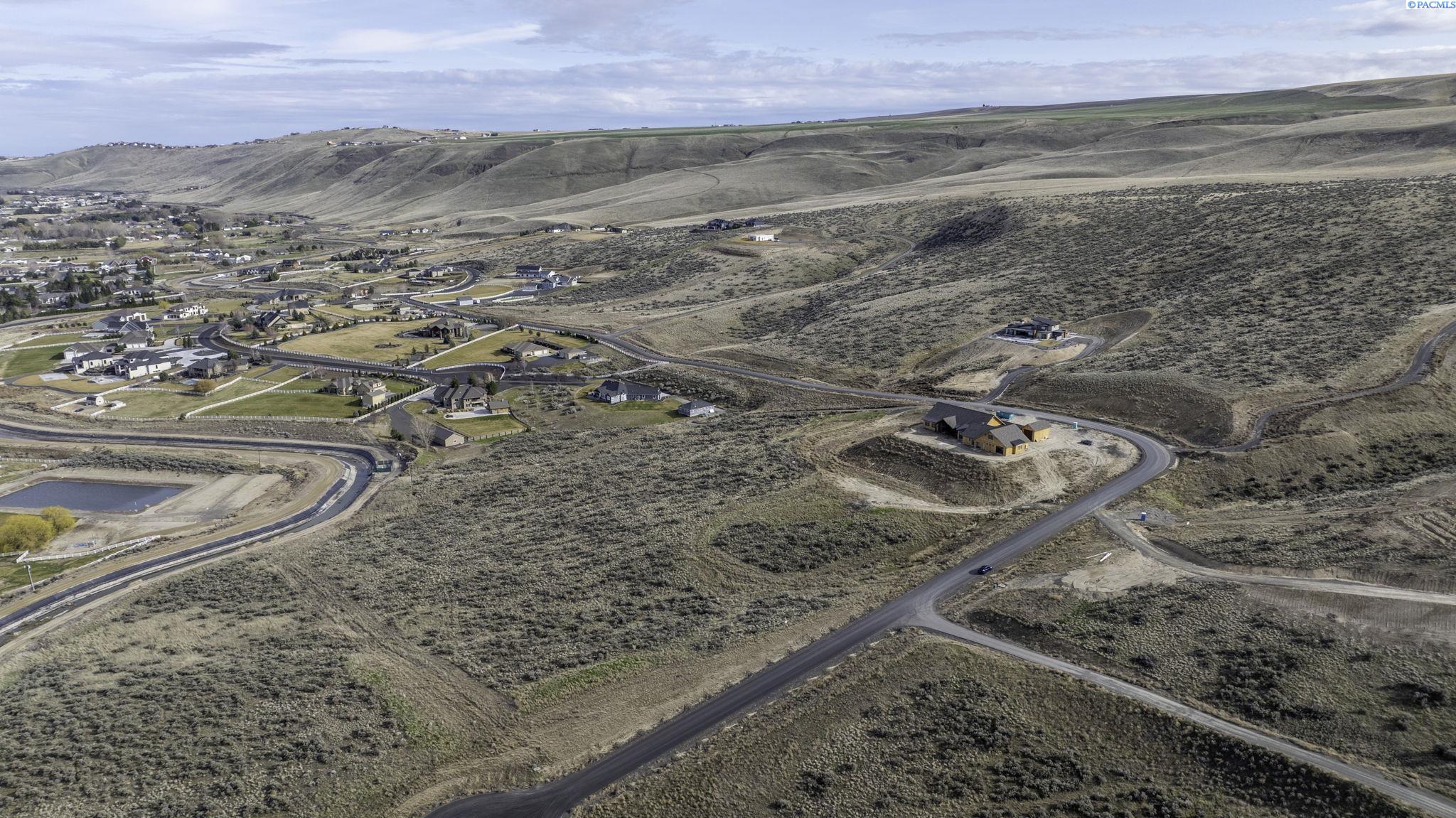Aerial view of a hillside home with a bare dirt yard, winding roads, and scattered neighboring homes.