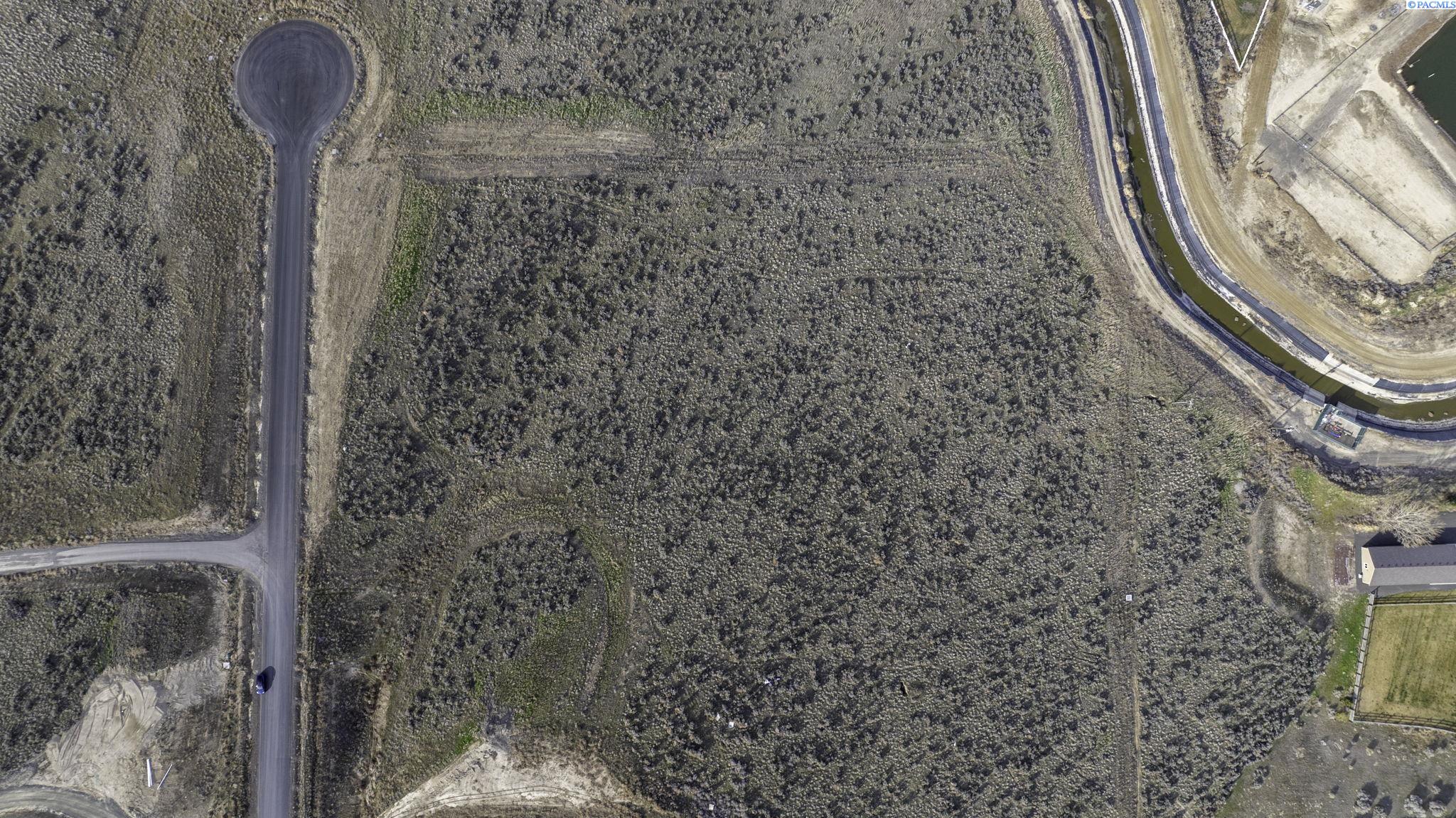 Aerial view of a vacant scrub-covered parcel beside a paved road and canal.