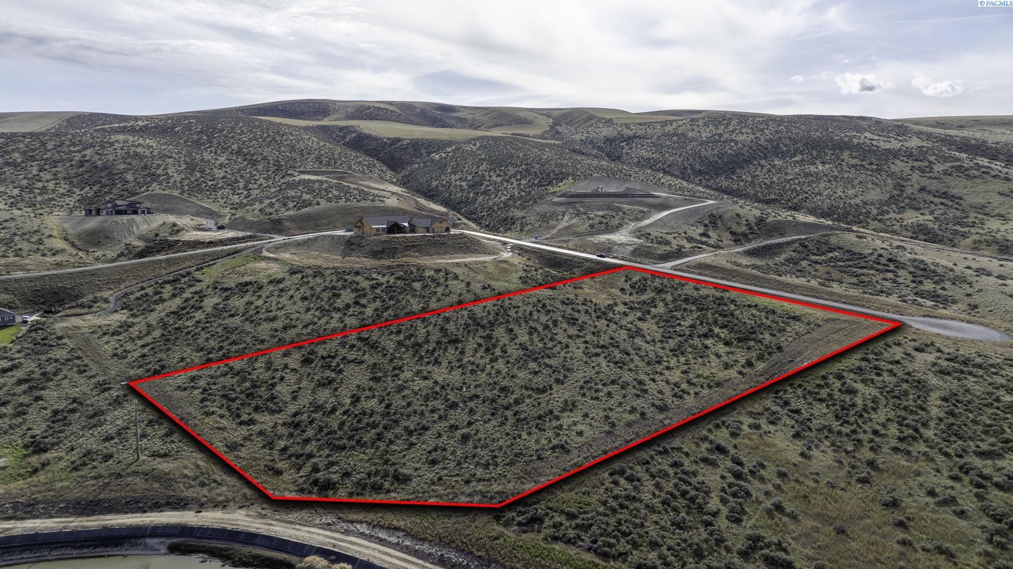Vacant scrub-covered parcel outlined in red, with a road and rolling hills beyond.