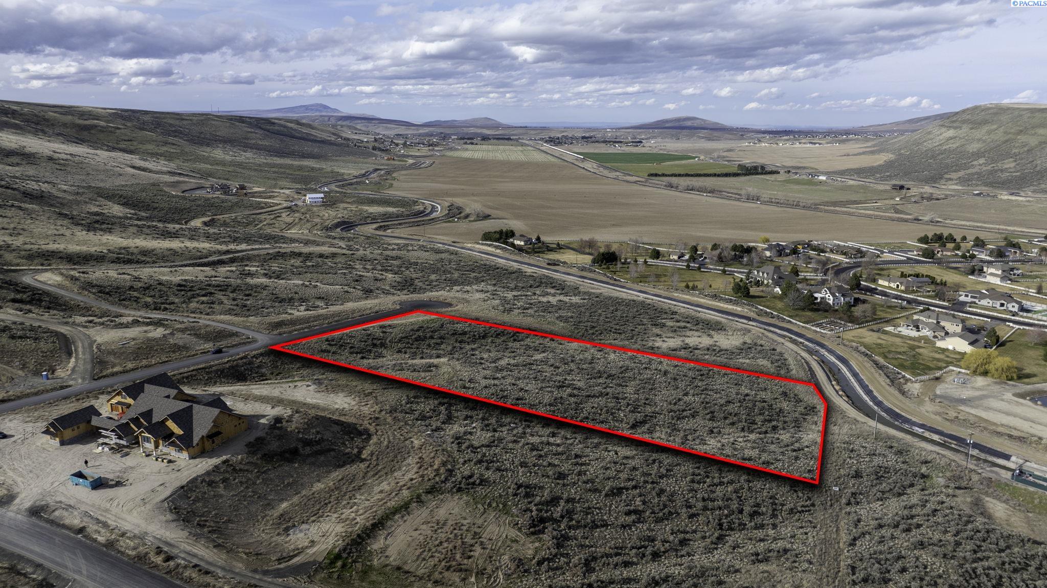 Aerial view of a brush-covered vacant parcel outlined in red, with homes and rolling hills nearby.
