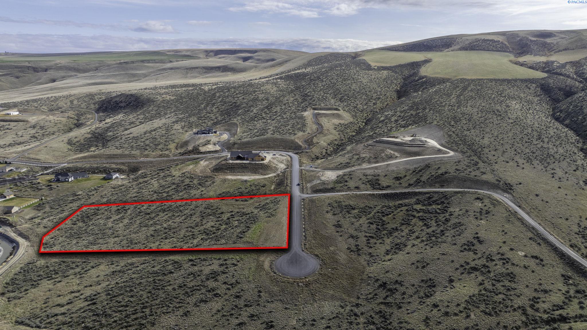Vacant hillside parcel outlined in red beside a paved road.