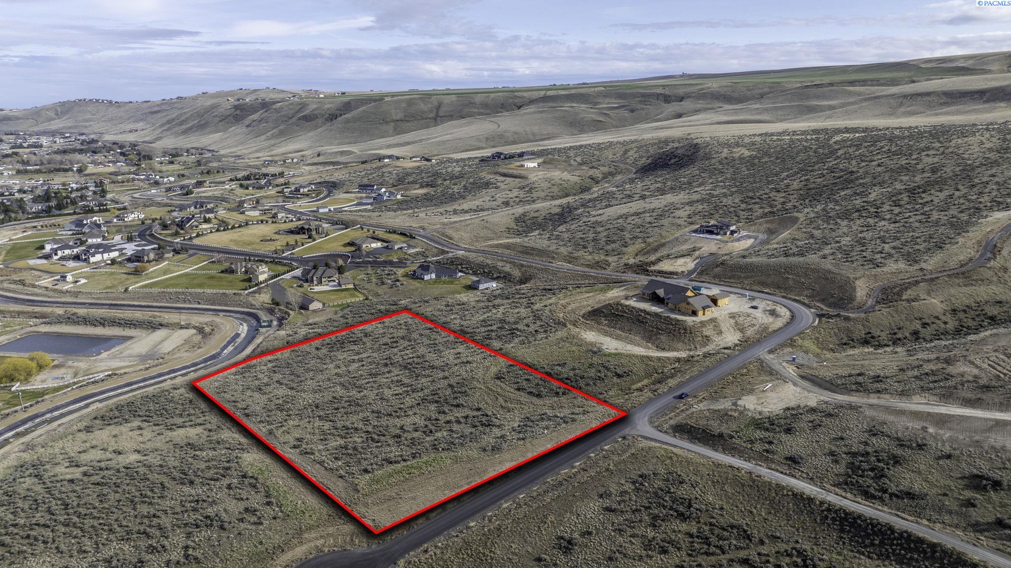 Aerial view of a scrub-covered vacant parcel outlined in red beside a road and nearby homes.