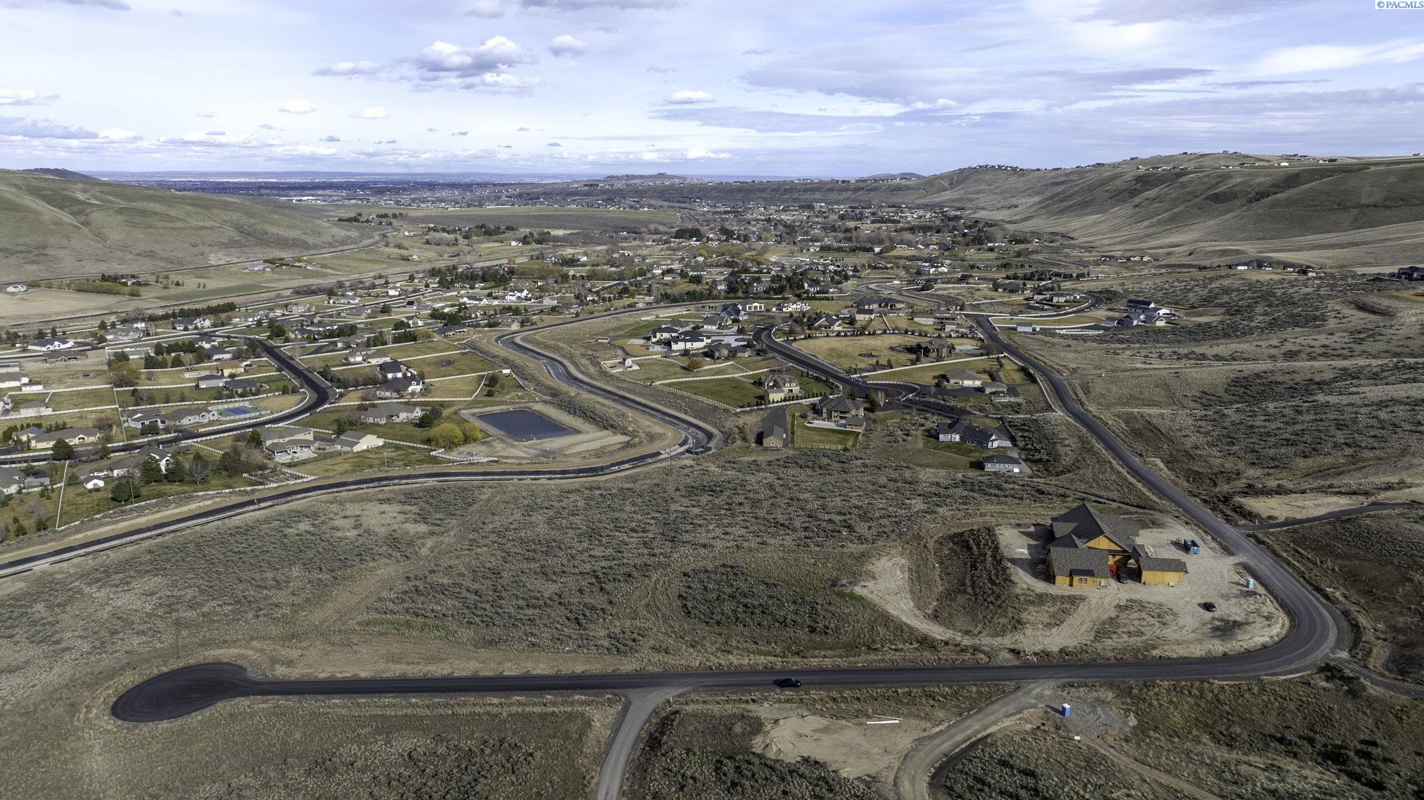Aerial view of a residential development amid rolling hills, with a house under construction in the foreground.