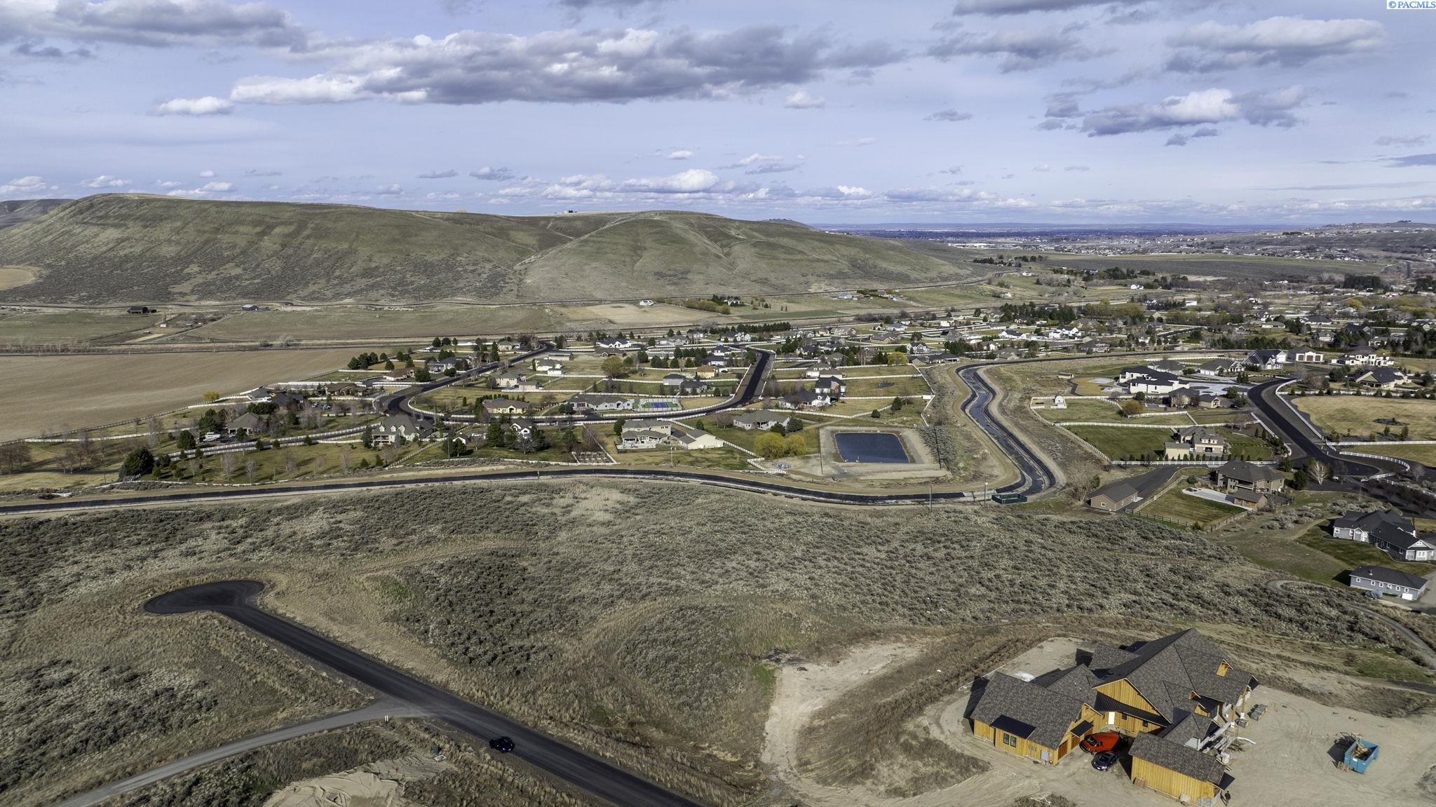 Aerial view of a residential development with winding roads, a small pond, and rolling hills.