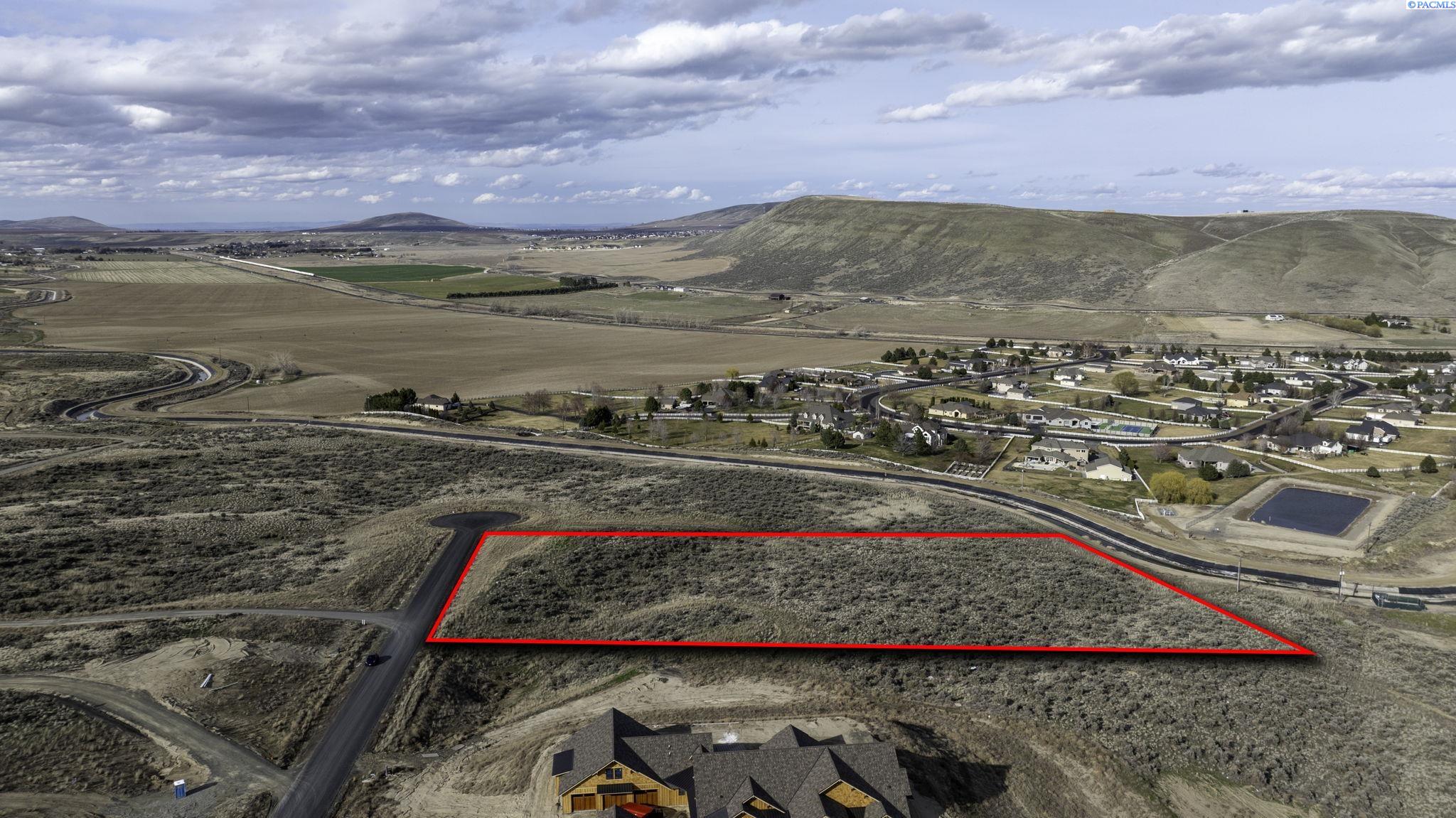 Aerial view of a scrub-covered vacant parcel outlined in red beside a road and residential development.