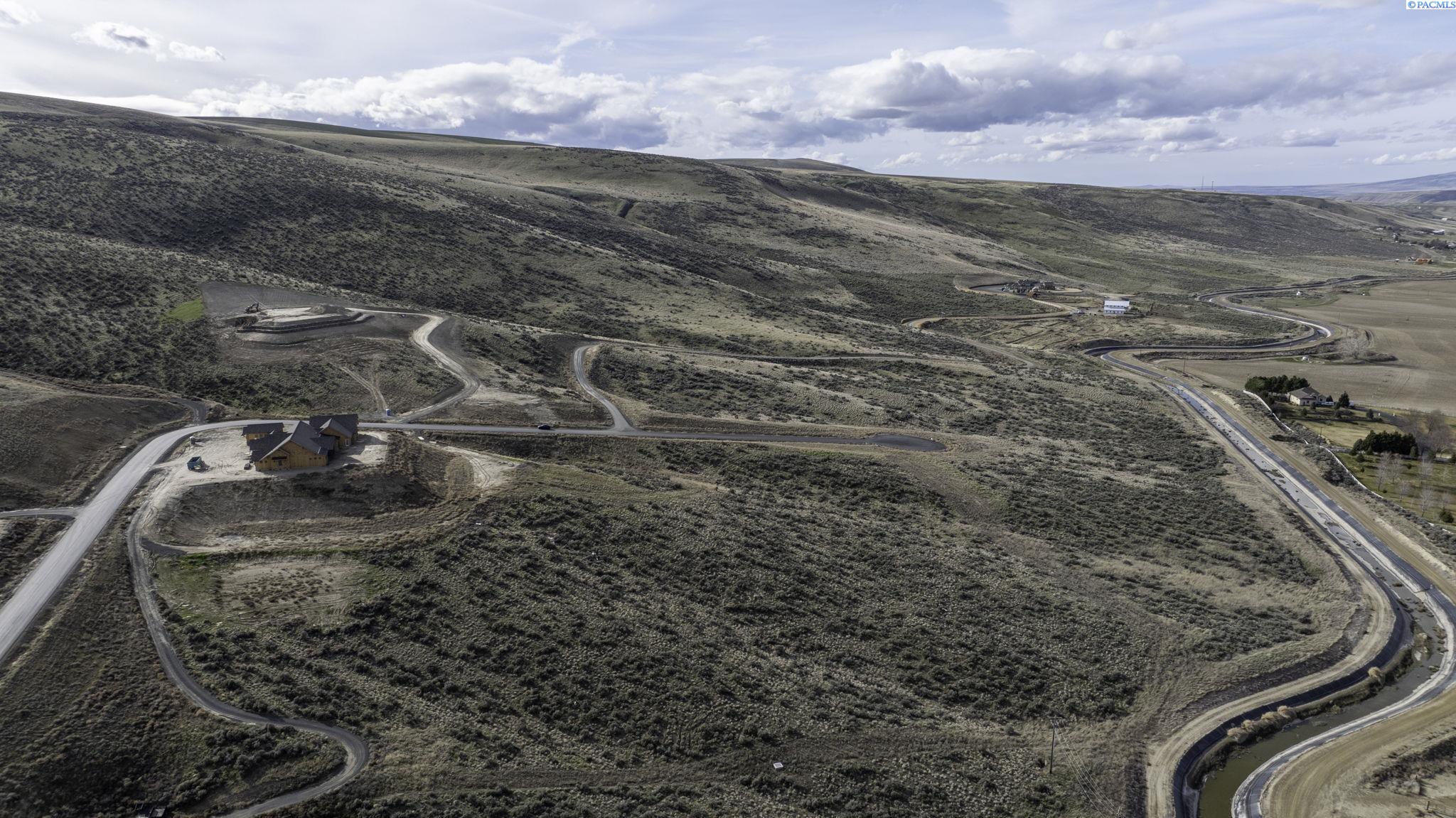 Aerial view of rolling scrubland and winding roads, with a house under construction near the left edge.