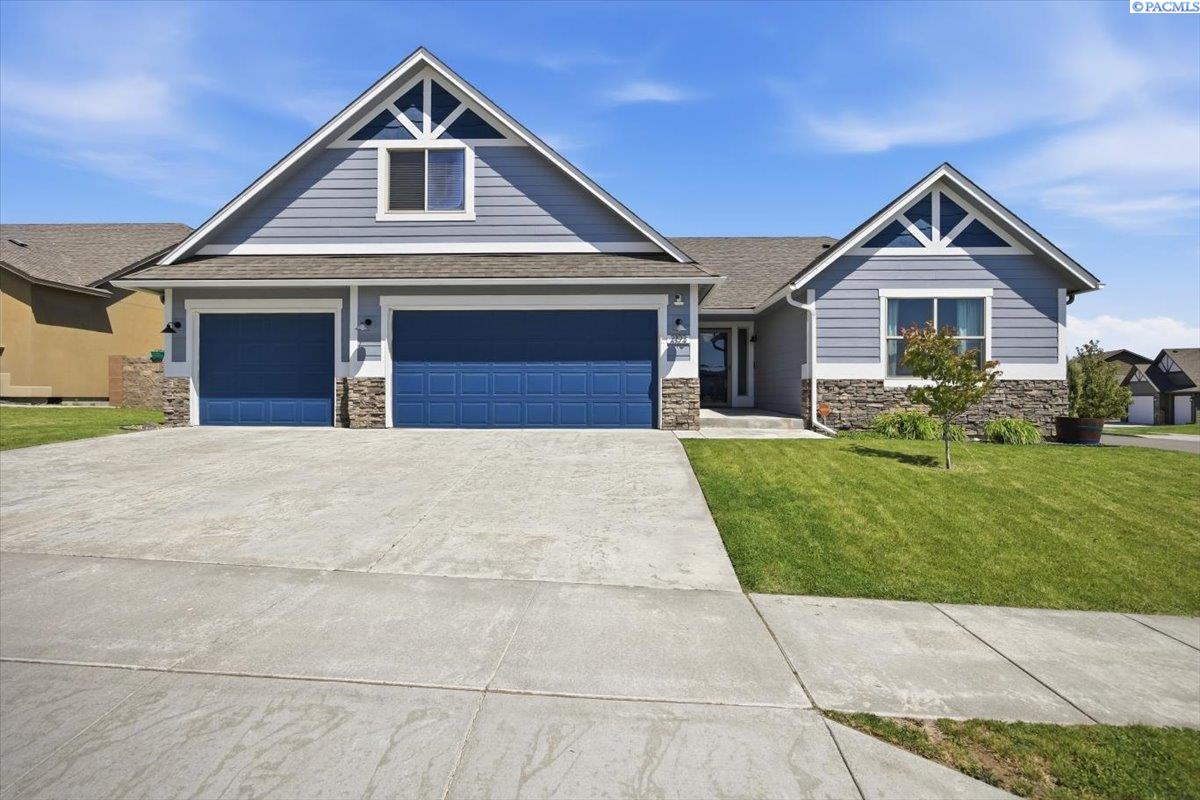 Gray gabled home with blue garage doors, stone accents, and a wide concrete driveway.
