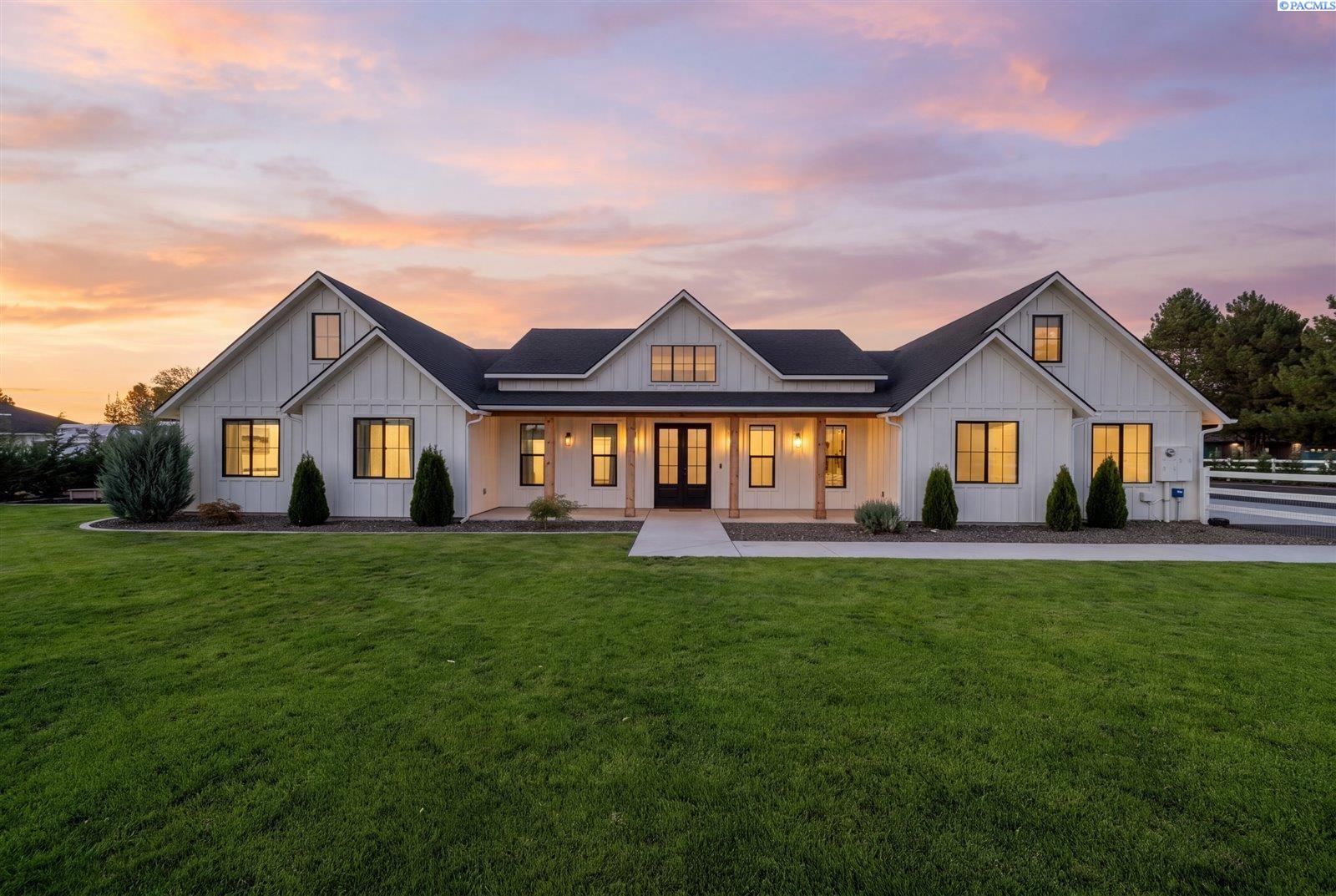 White farmhouse with multiple gables and illuminated windows beneath a colorful dusk sky.