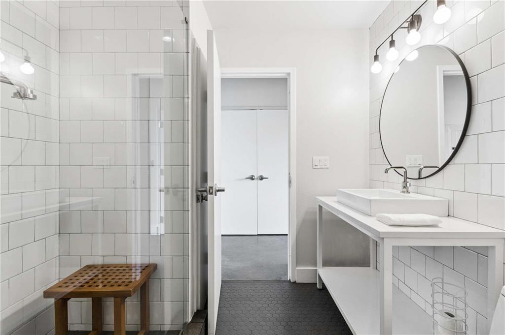 Bathroom with glass shower, white subway tile, round mirror, and white vanity.