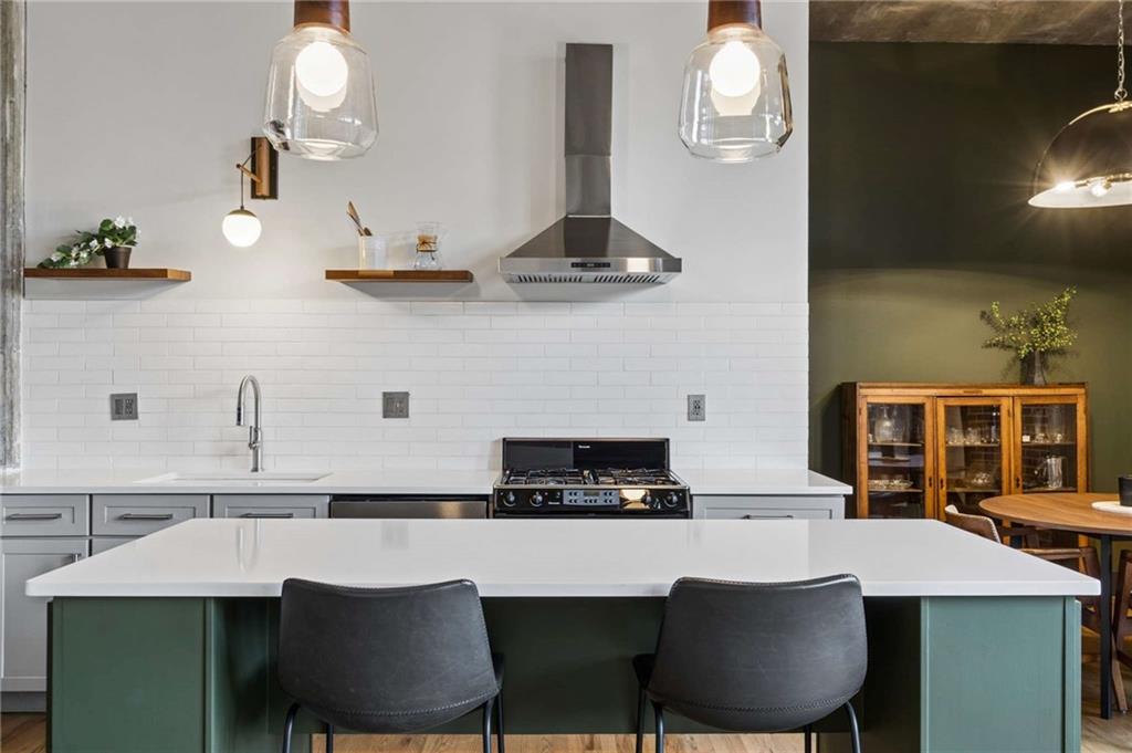Modern kitchen with a white island, green cabinetry, and stainless-steel range.