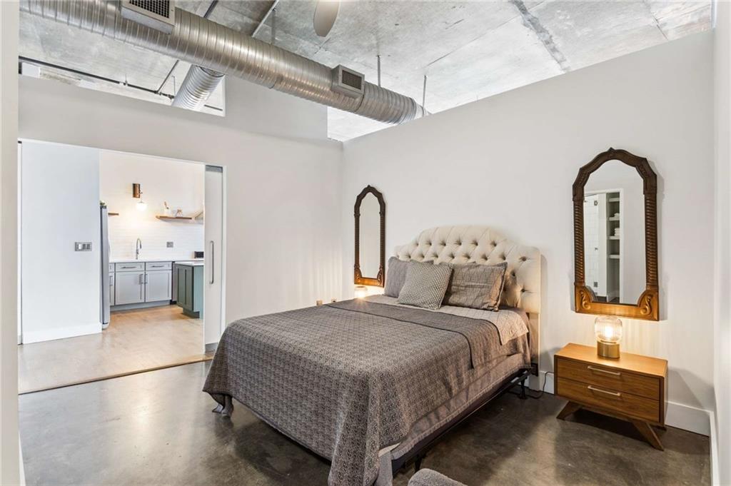 Loft-style bedroom with a tufted bed, ornate mirrors, exposed concrete ceiling, and open doorway to the kitchen.